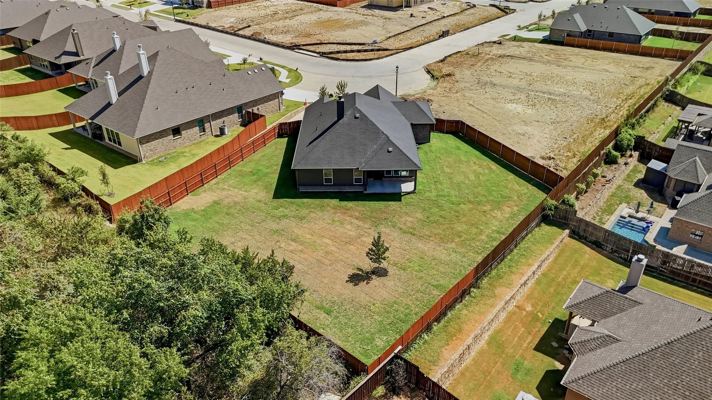 Expansive fenced backyard with a patio and a single-story residence featuring a dark shingle roof