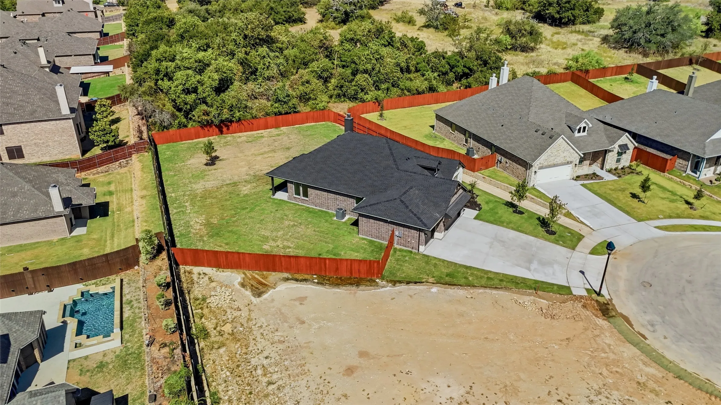 Expansive property featuring a red-stained privacy fence, a large grassy yard, and a paved driveway