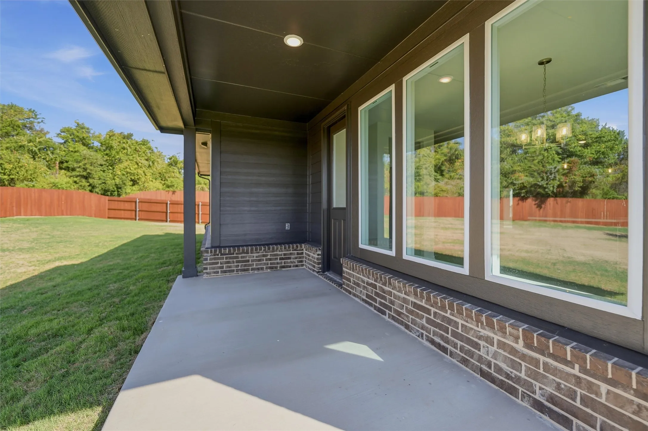 Covered patio with a concrete surface, brick foundation, multiple large windows, exterior siding, and a wooden fence