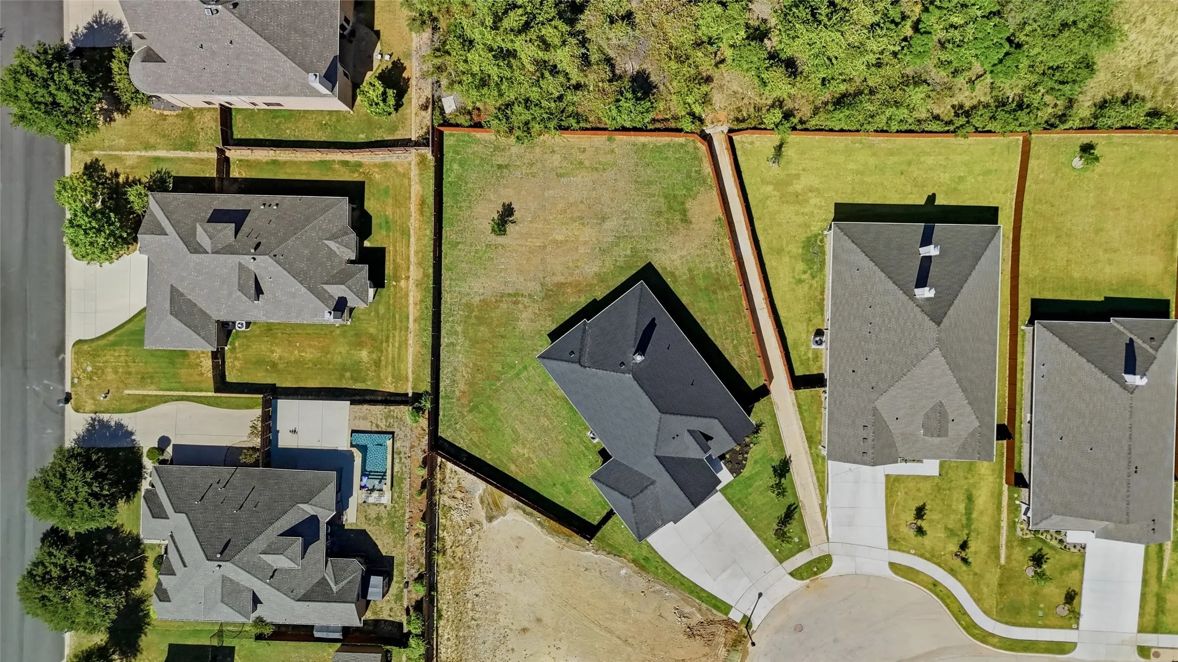 Expansive lot featuring a residential structure with an attached driveway, surrounded by green spaces and mature trees