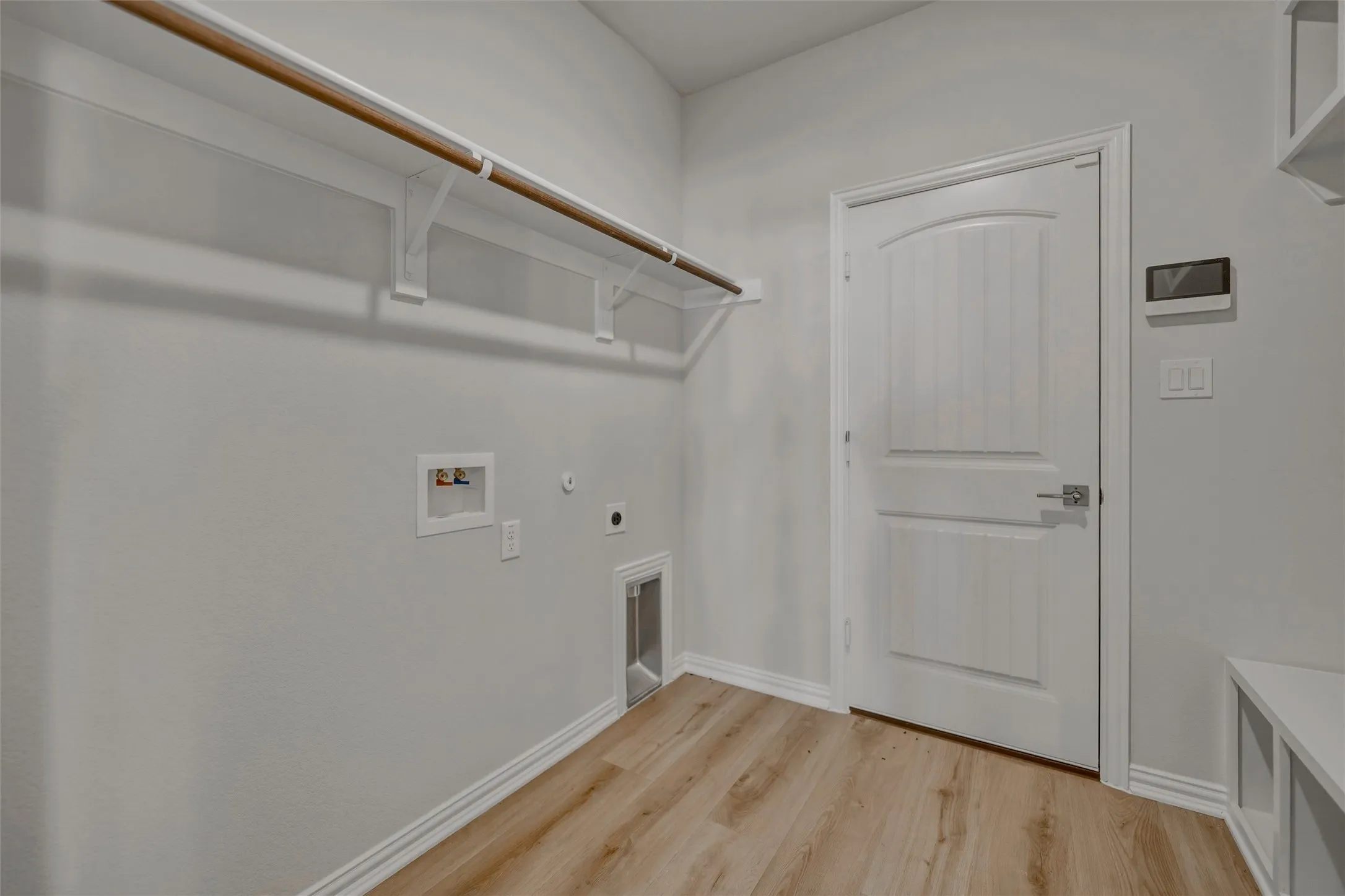 Wood-finish flooring with white baseboards, dedicated laundry connections, and a built-in hanging rod