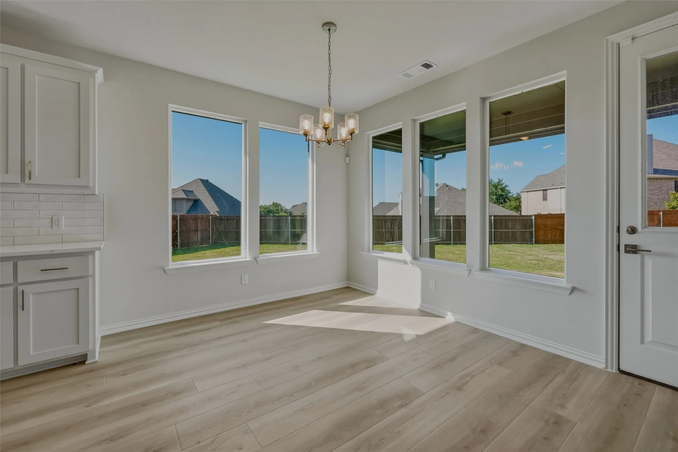Wood-finish flooring, white shaker cabinetry, subway tile backsplash, multiple large windows, and an overhead chandelier