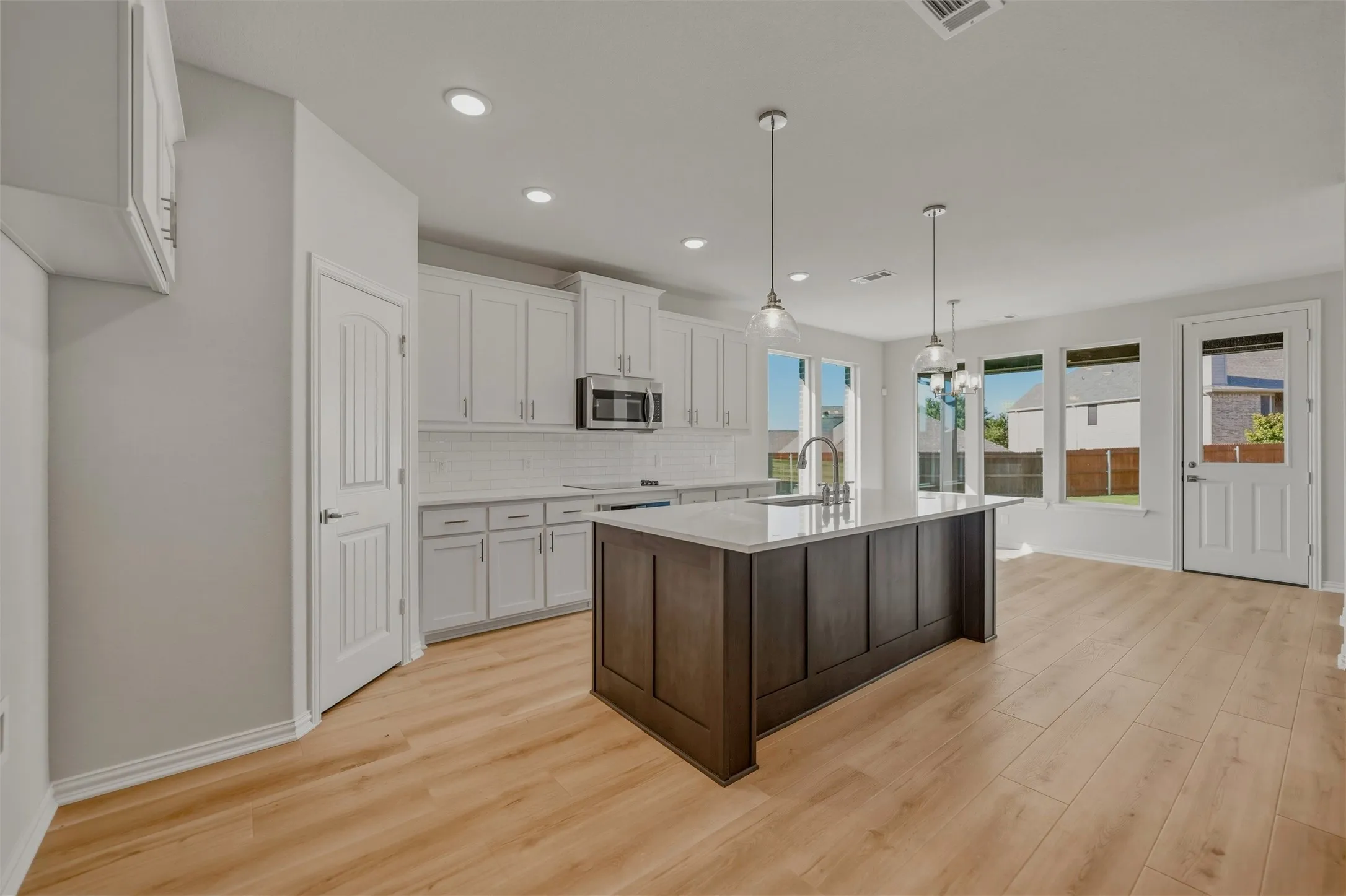 Spacious kitchen featuring an expansive center island, white cabinetry, integrated stainless steel appliances, and wood-finish flooring