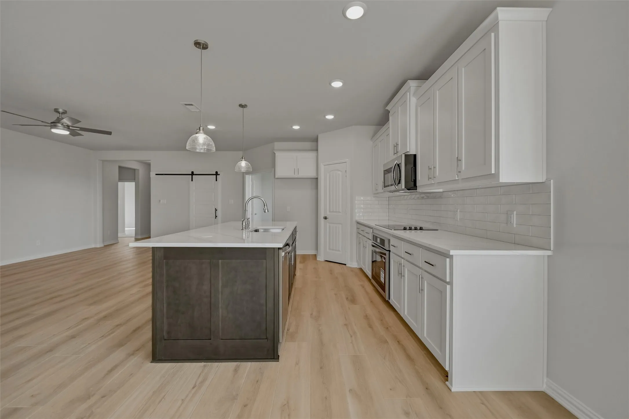 Open-concept kitchen with a central island, stainless steel appliances, white subway tile backsplash, and light wood-finish flooring