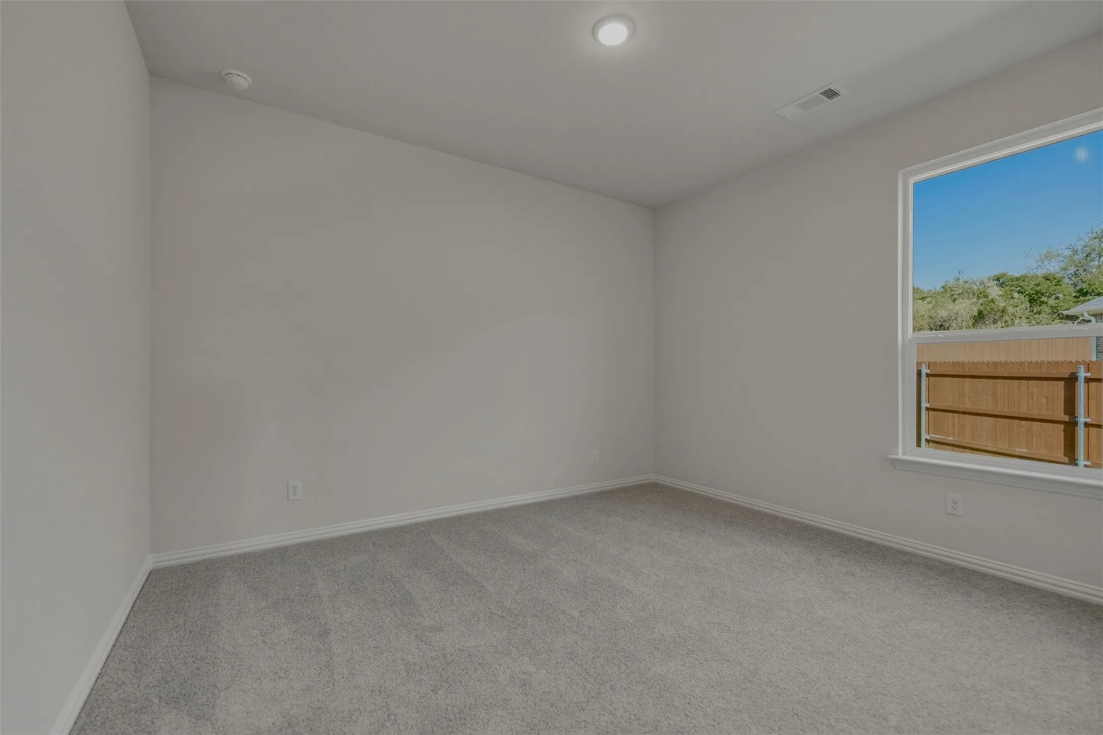 Recessed ceiling lighting, light gray wall paint, gray carpet, white trim, and a window with outdoor scenery