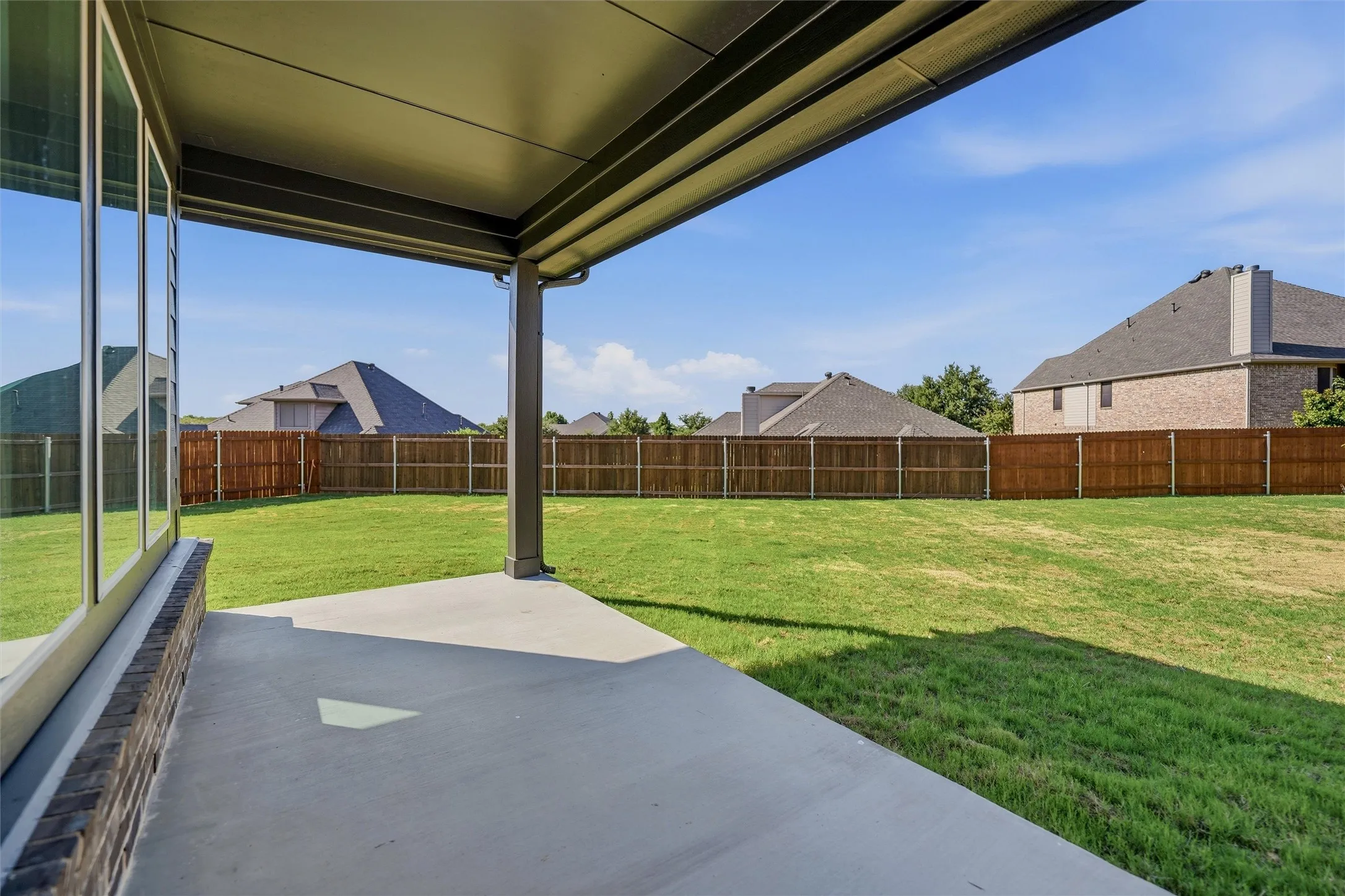 Expansive backyard with a manicured lawn, full privacy fencing, and a covered concrete patio