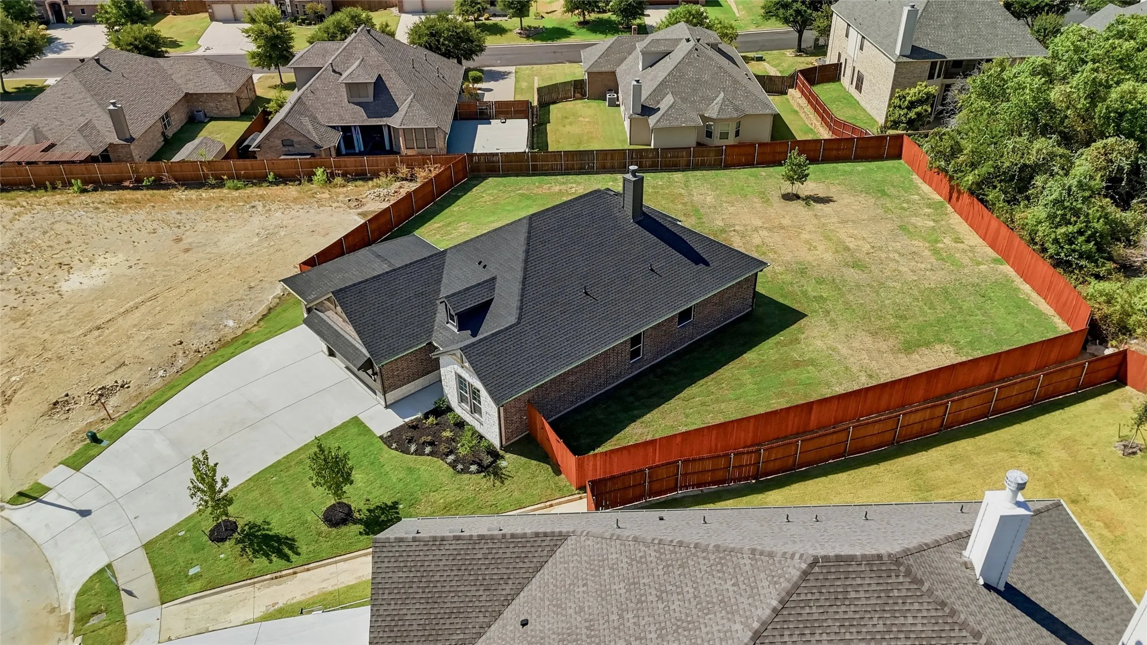 Expansive fenced yard with mature trees, long concrete driveway, and attached two-car garage