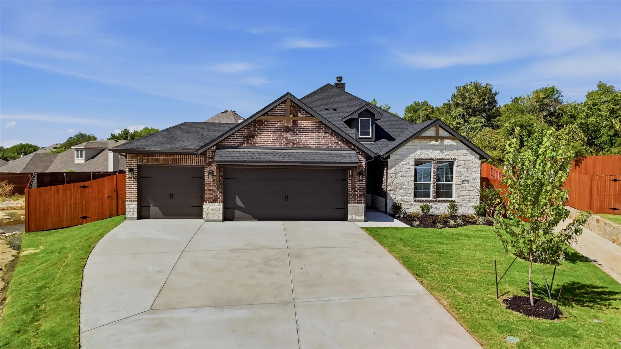 Multi-material exterior with brick and stone accents, dark garage doors, concrete driveway, and manicured landscaping
