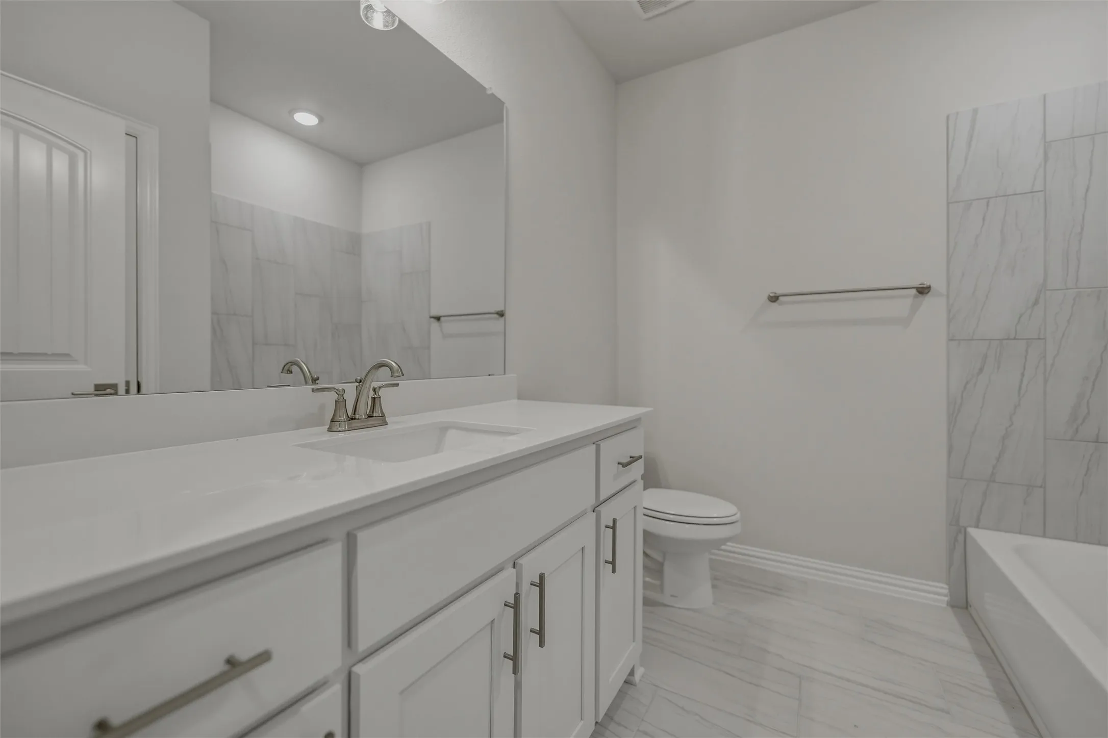 White vanity with an integrated sink, brushed nickel faucet, large mirror, and tiled shower surround