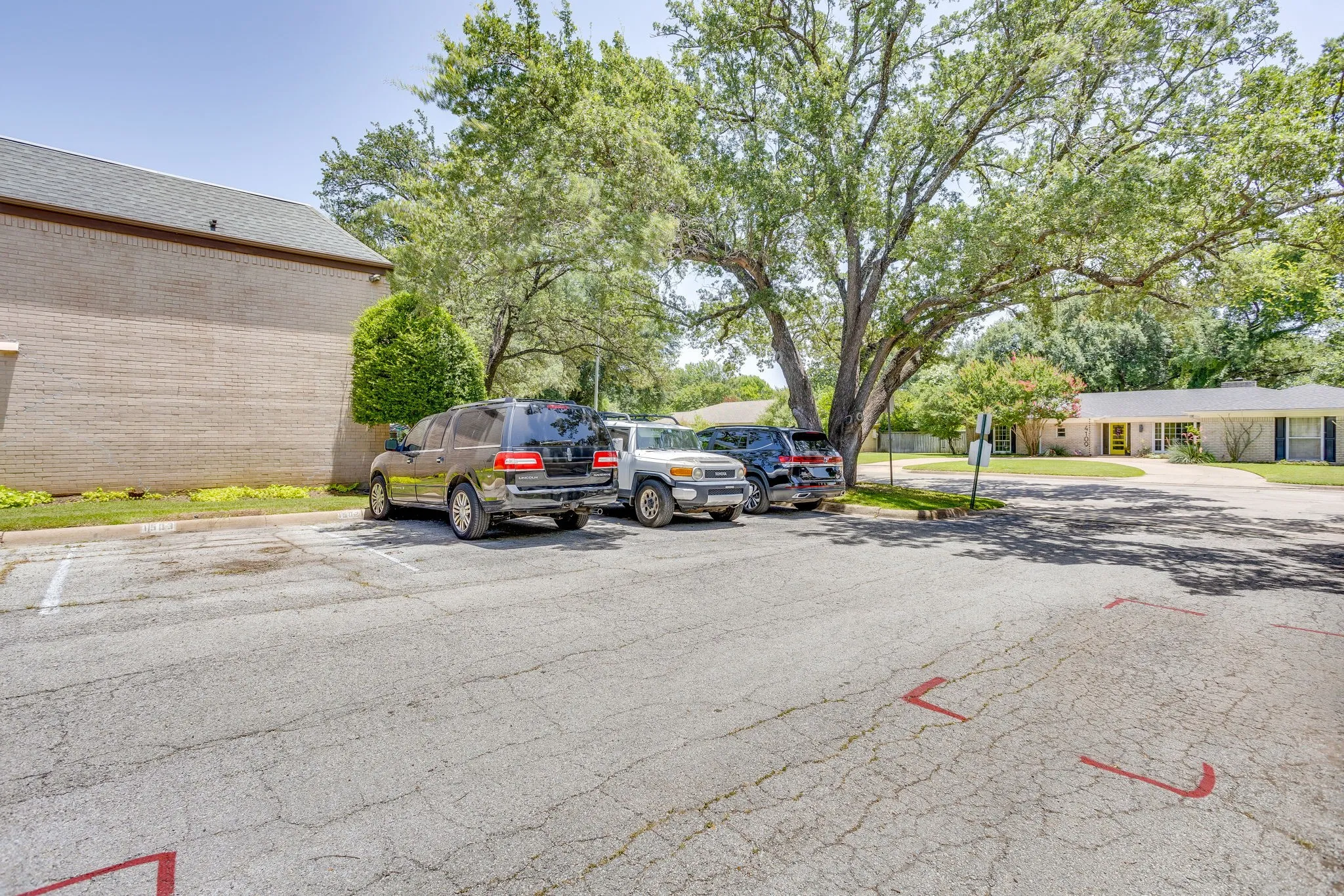 Paved parking area featuring multiple designated parking spaces, surrounded by mature trees and landscaping