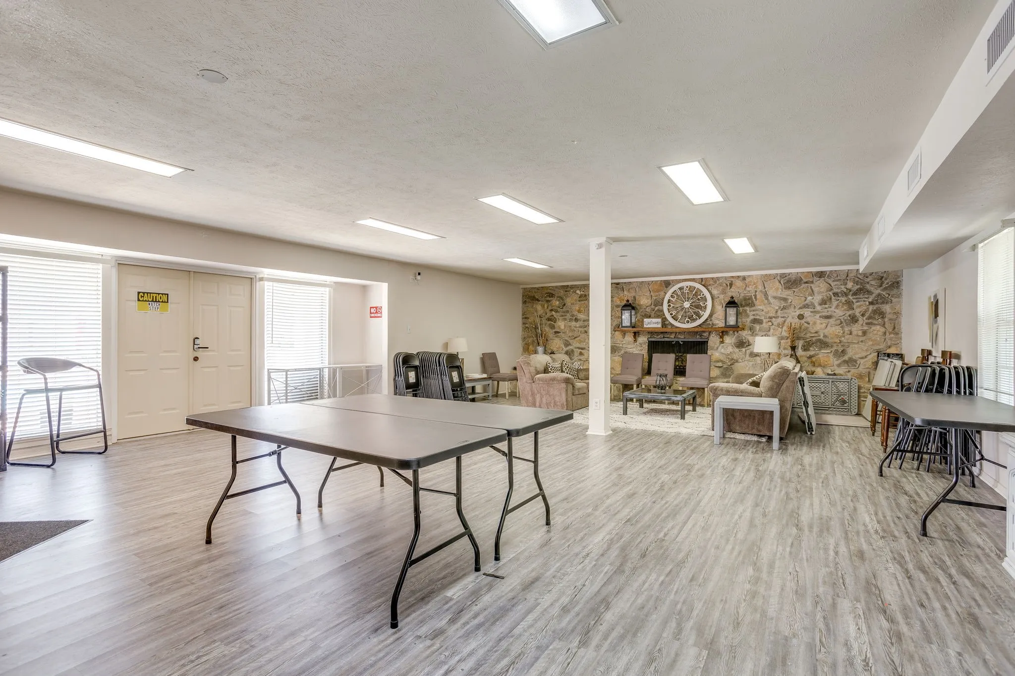 Spacious multi-purpose room featuring wood-finish flooring, recessed lighting, and a stone accent wall with a built-in fireplace, Community rec room by the pool