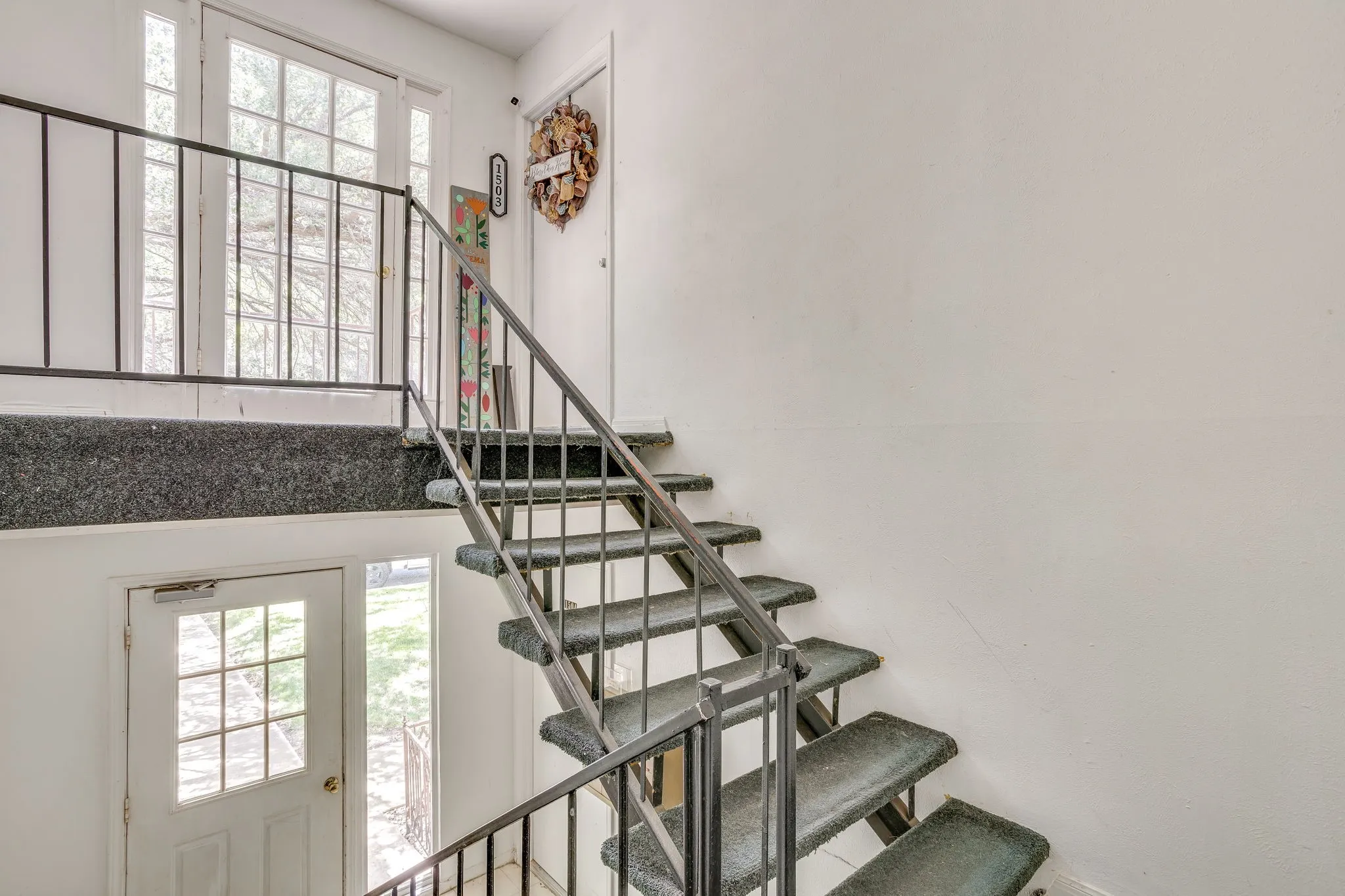 Multi-level interior featuring a carpeted staircase with metal railings, white walls, and glass-paned doors providing natural light