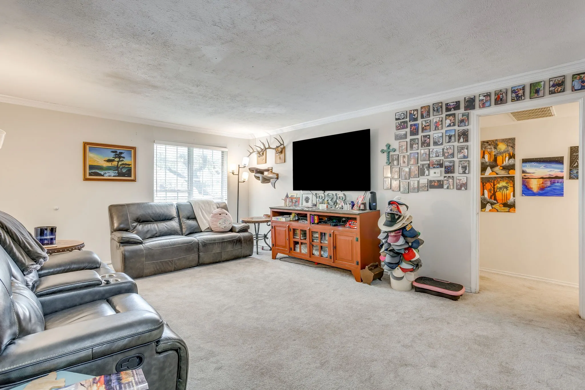 Living area featuring light-toned carpeting, a window with horizontal blinds, and crown molding