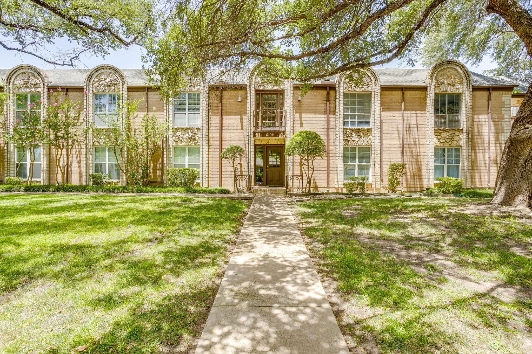 Brick facade building with a central entryway, decorative arched window surrounds, and a concrete pathway
