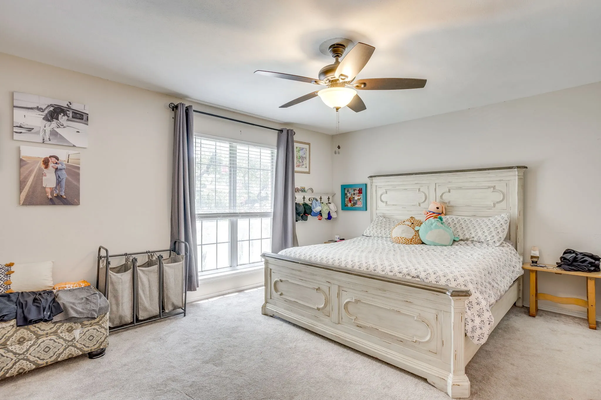 Carpeted bedroom featuring a large window with blinds and drapes, a ceiling fan with integrated lighting, and neutral wall tones