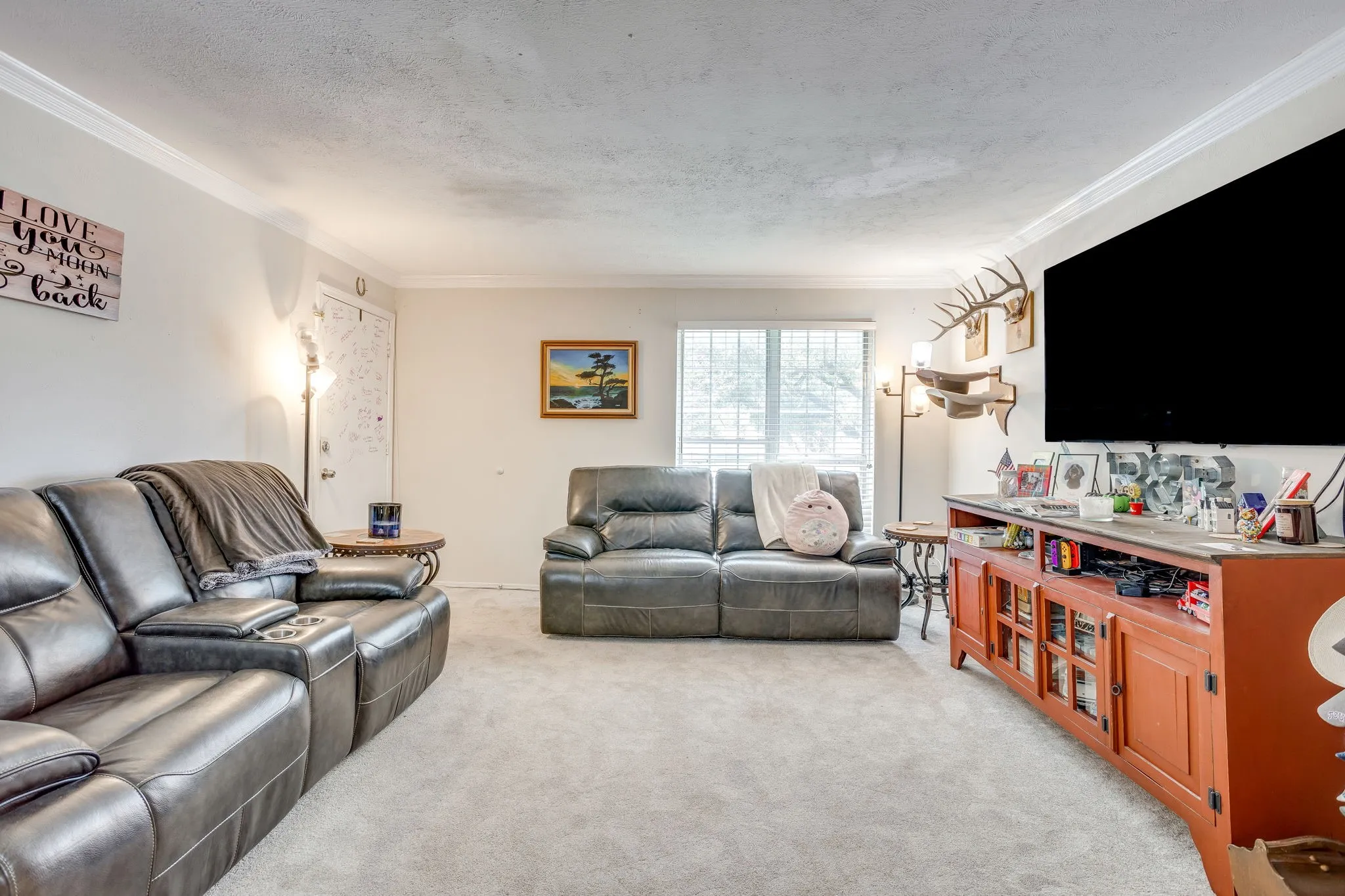 Carpeted living area featuring white walls, crown molding, and a built-in entertainment console