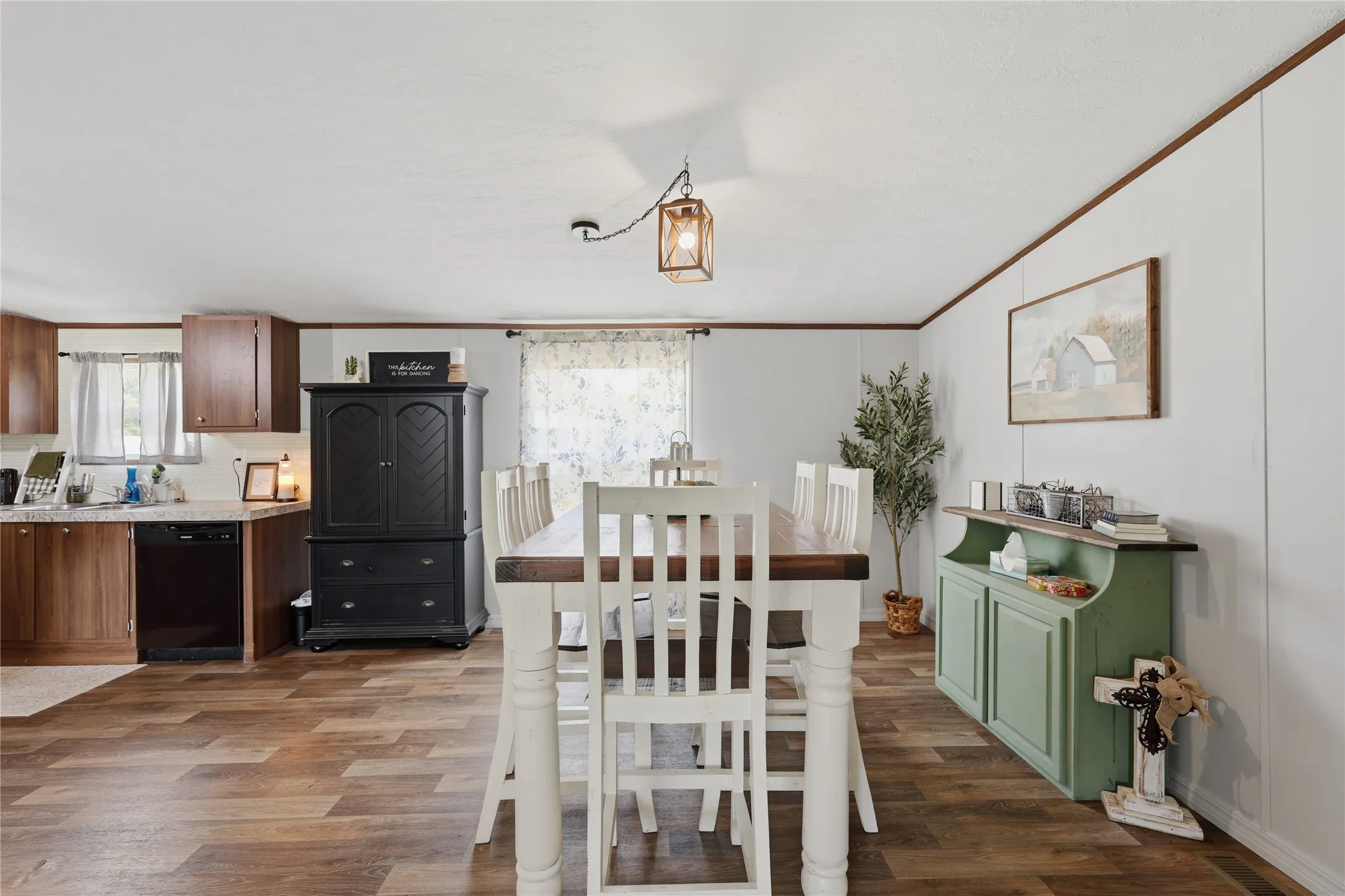Open concept living space featuring wood-finish flooring, white panel walls, and a visible kitchen area with wood cabinetry