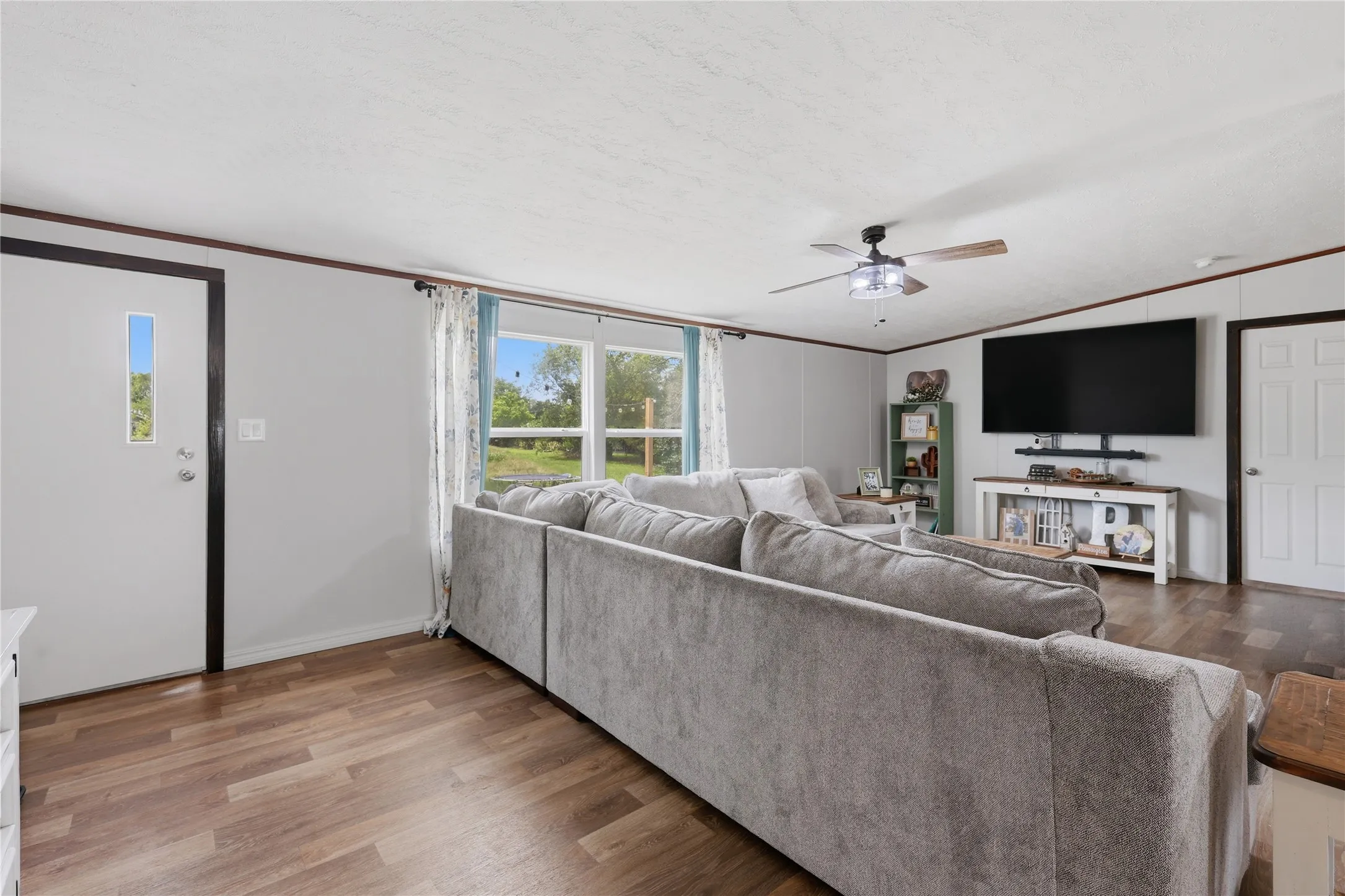 Spacious living area featuring wood-finish flooring, a contemporary ceiling fan, and multiple windows