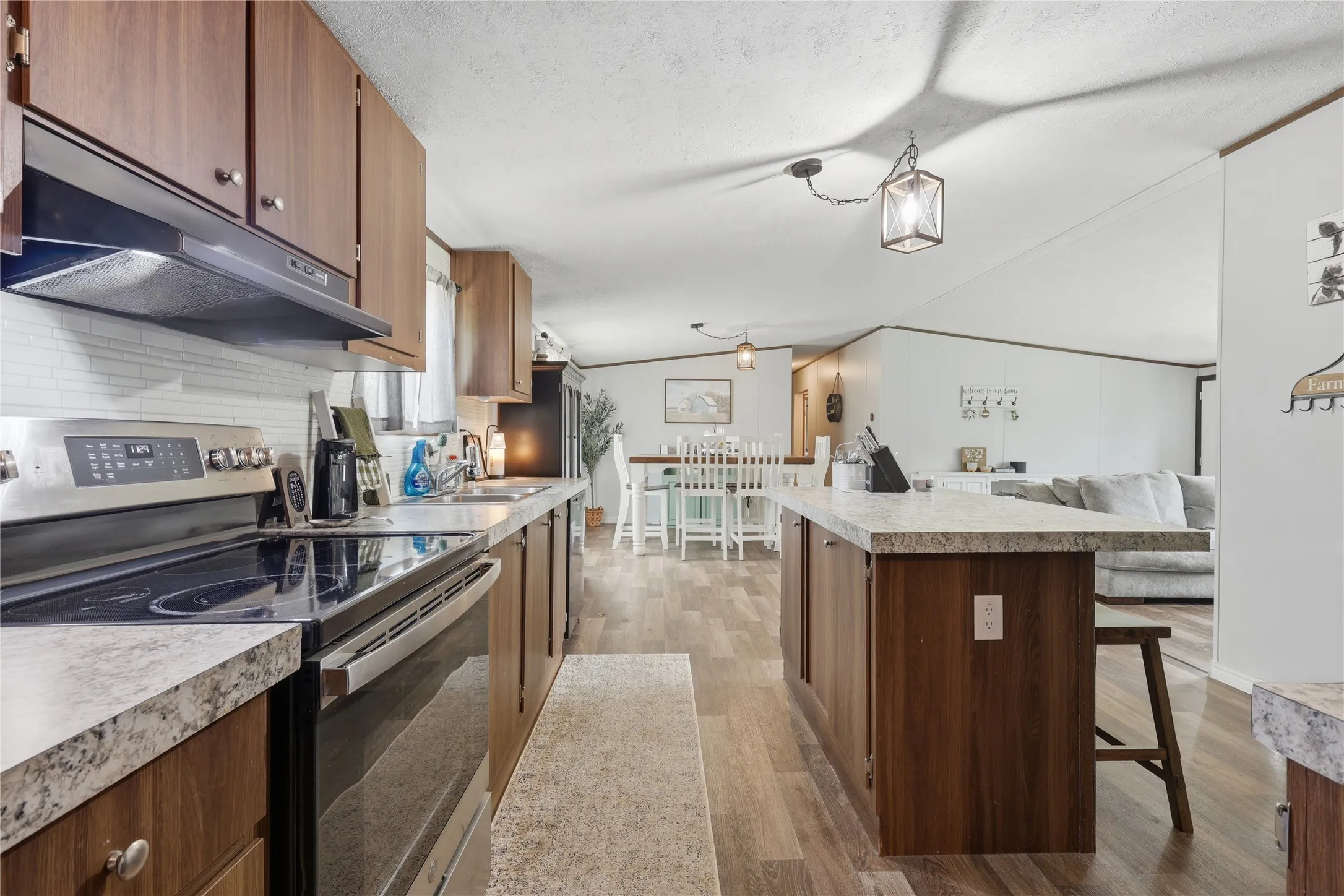 Open-concept kitchen featuring wood-finish cabinetry, stainless steel appliances, and a tile backsplash