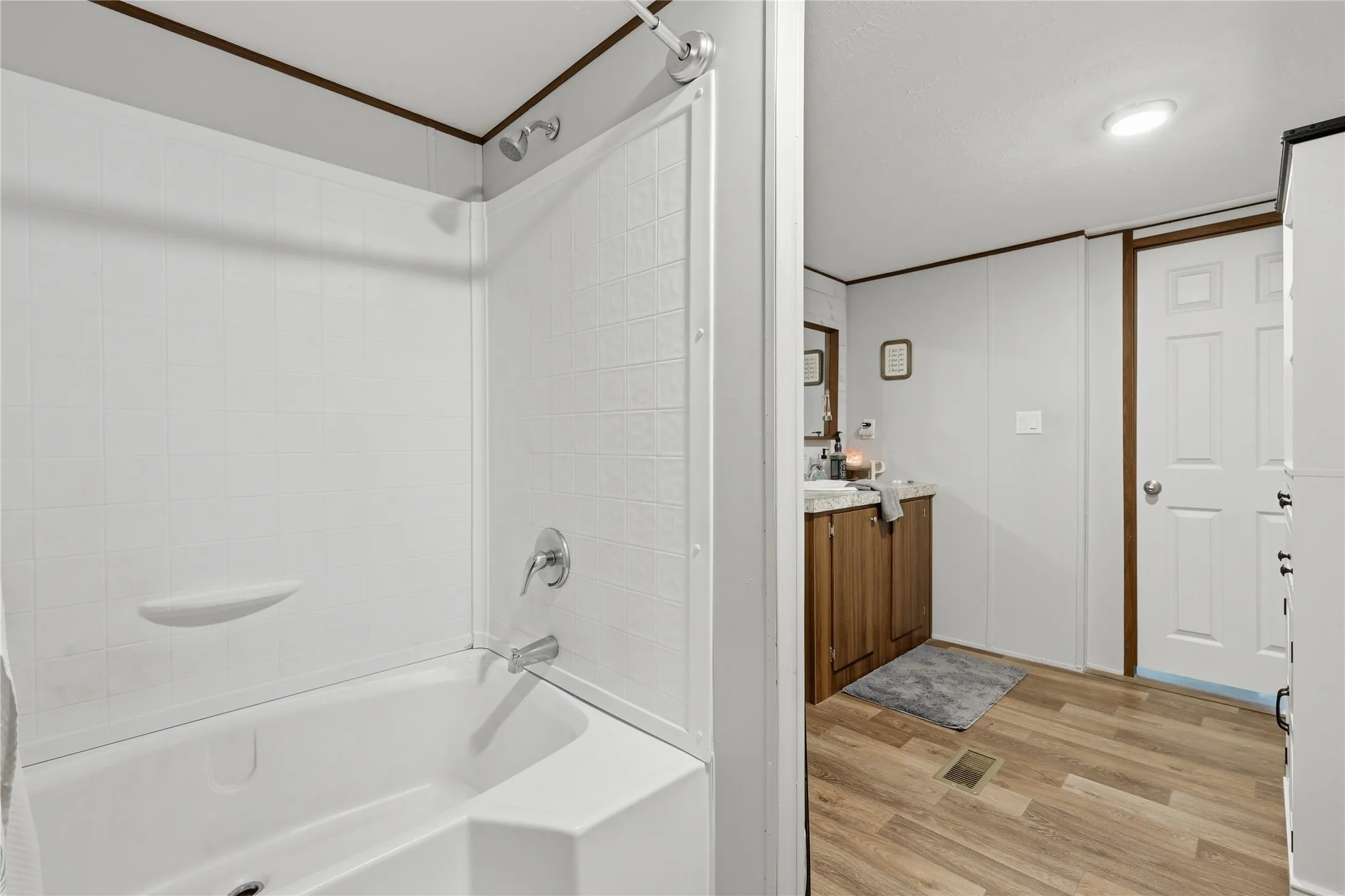 Bathroom featuring a white tub-shower combination with chrome fixtures, wood-finish flooring, a vanity with a white countertop and wood-finish cabinetry, and a surface-mounted ceiling light