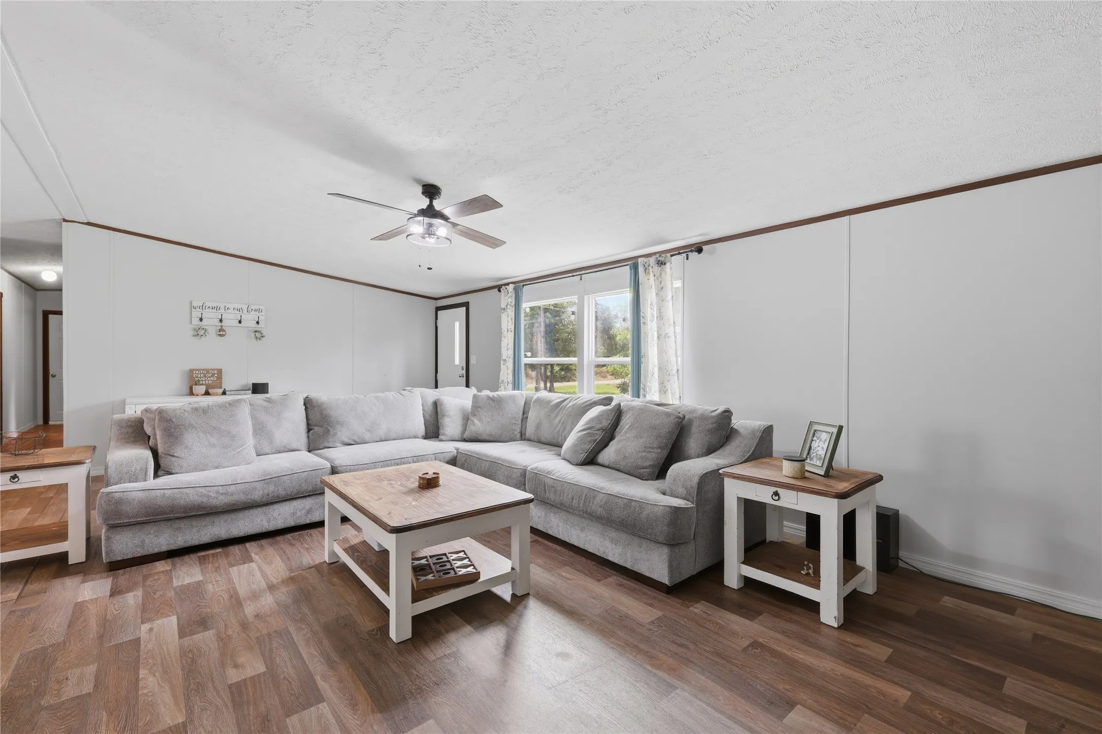 Spacious living area featuring wood-finish flooring, a ceiling fan with integrated lighting, and a prominent front door with an upper window