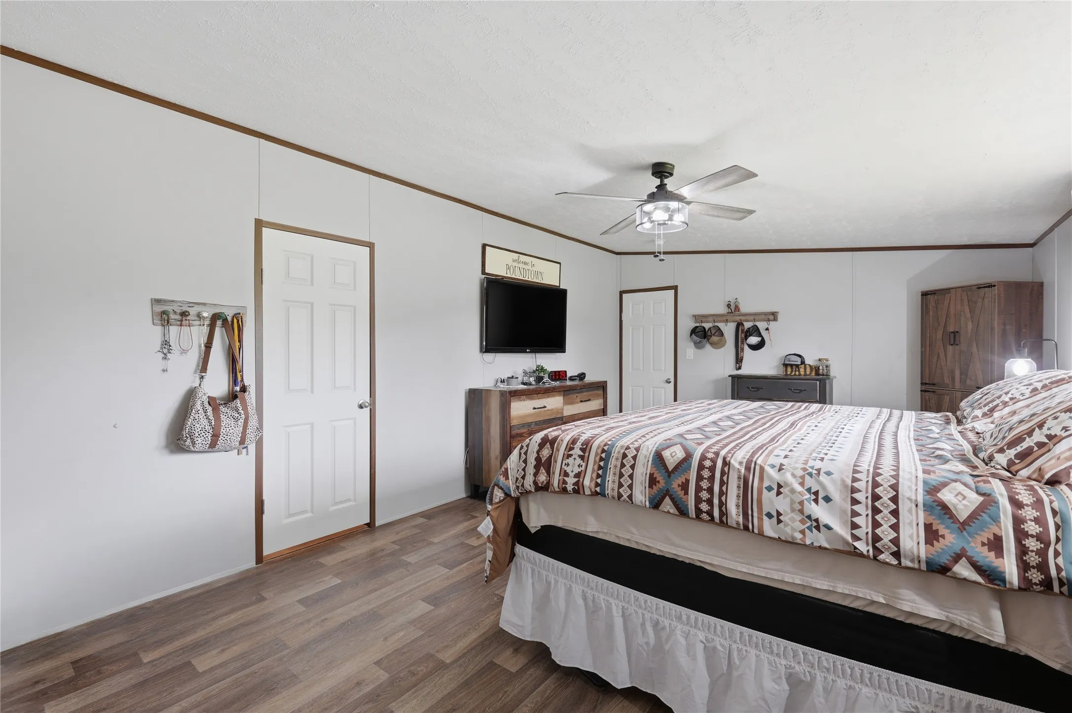 Room featuring wood-finish flooring, white paneled walls, and a ceiling fan with integrated lighting