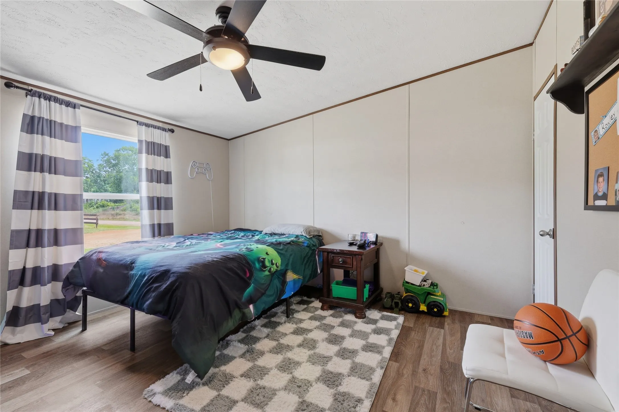 Bedroom featuring a ceiling fan with integrated lighting, wood-finish flooring, and a window providing natural light