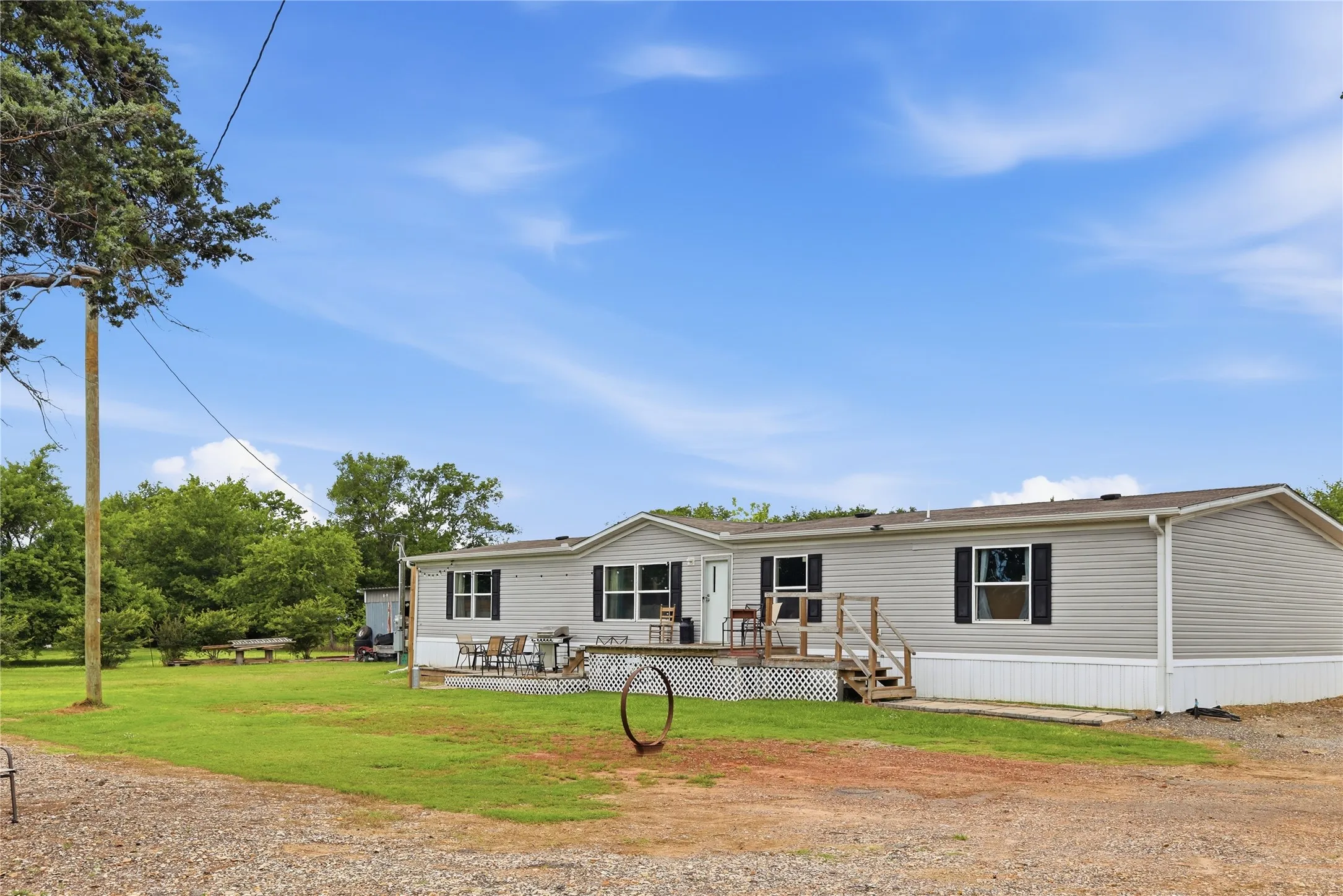 Spacious residence featuring light-colored siding, dark window shutters, and a front deck with lattice skirting