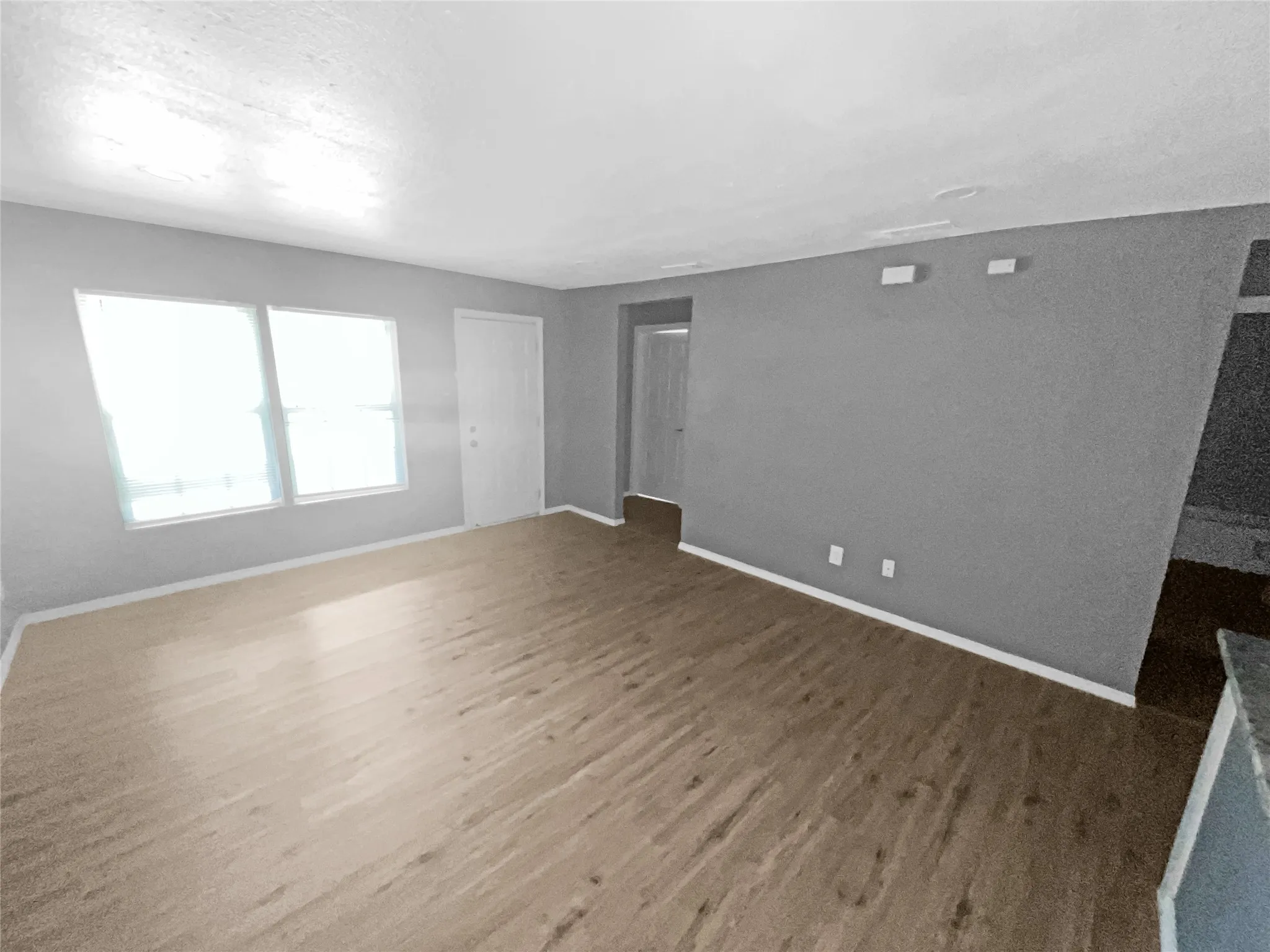 Spacious room featuring wood-finish flooring, two windows with blinds, gray wall paint, and white trim