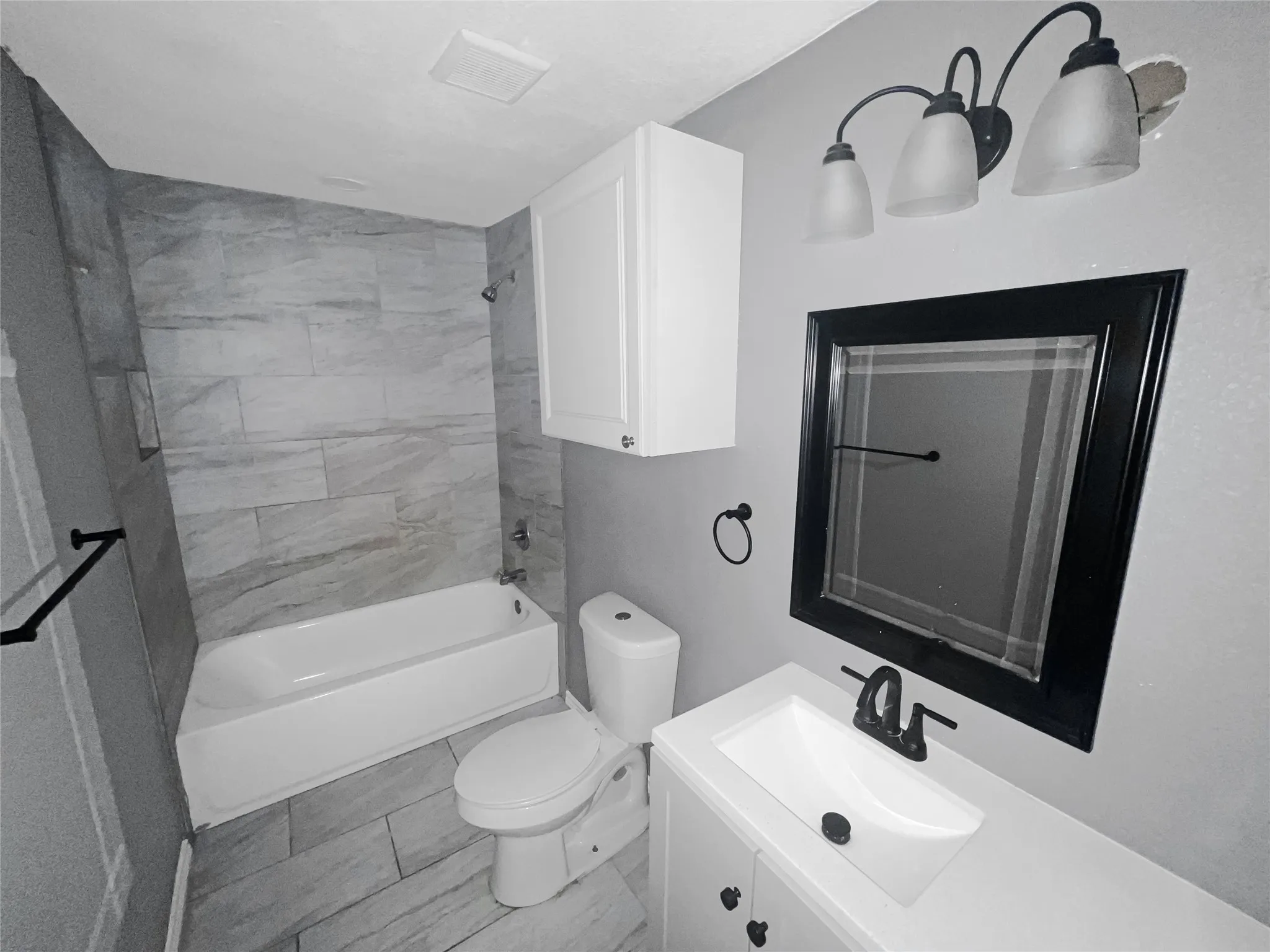 Contemporary bathroom featuring a white vanity with integrated sink, a dark framed mirror, and a three-light vanity fixture