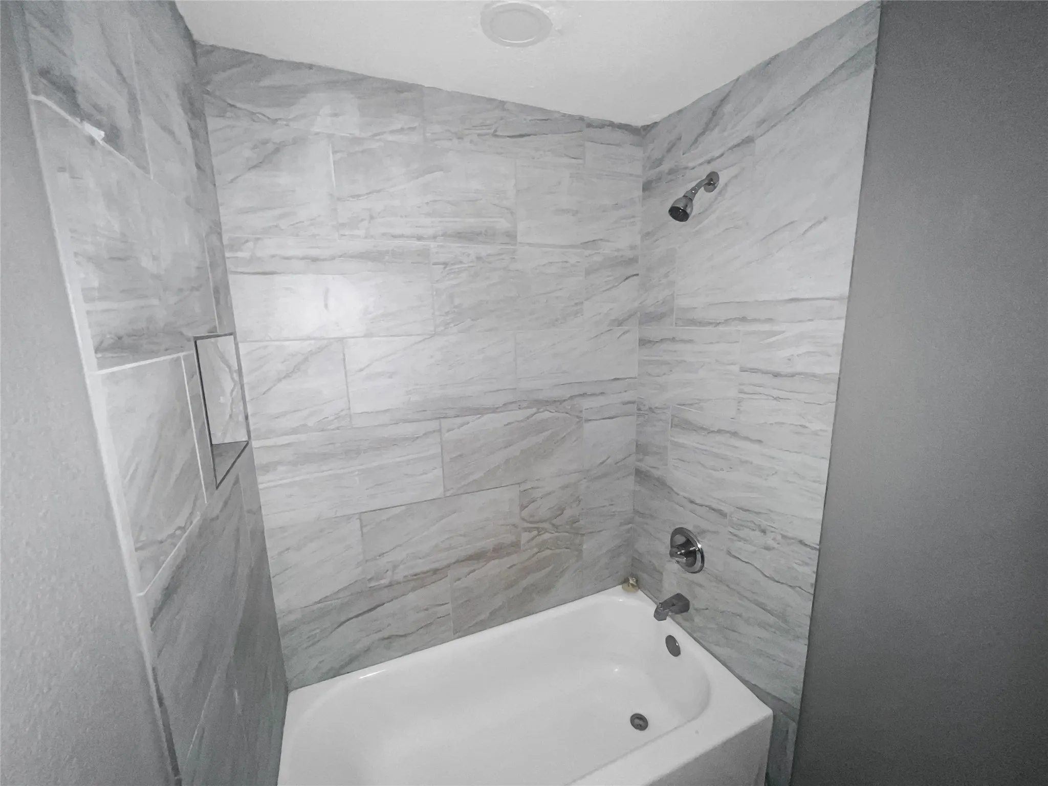 Full bath featuring a white tub, chrome showerhead, and a tiled surround with a built-in niche