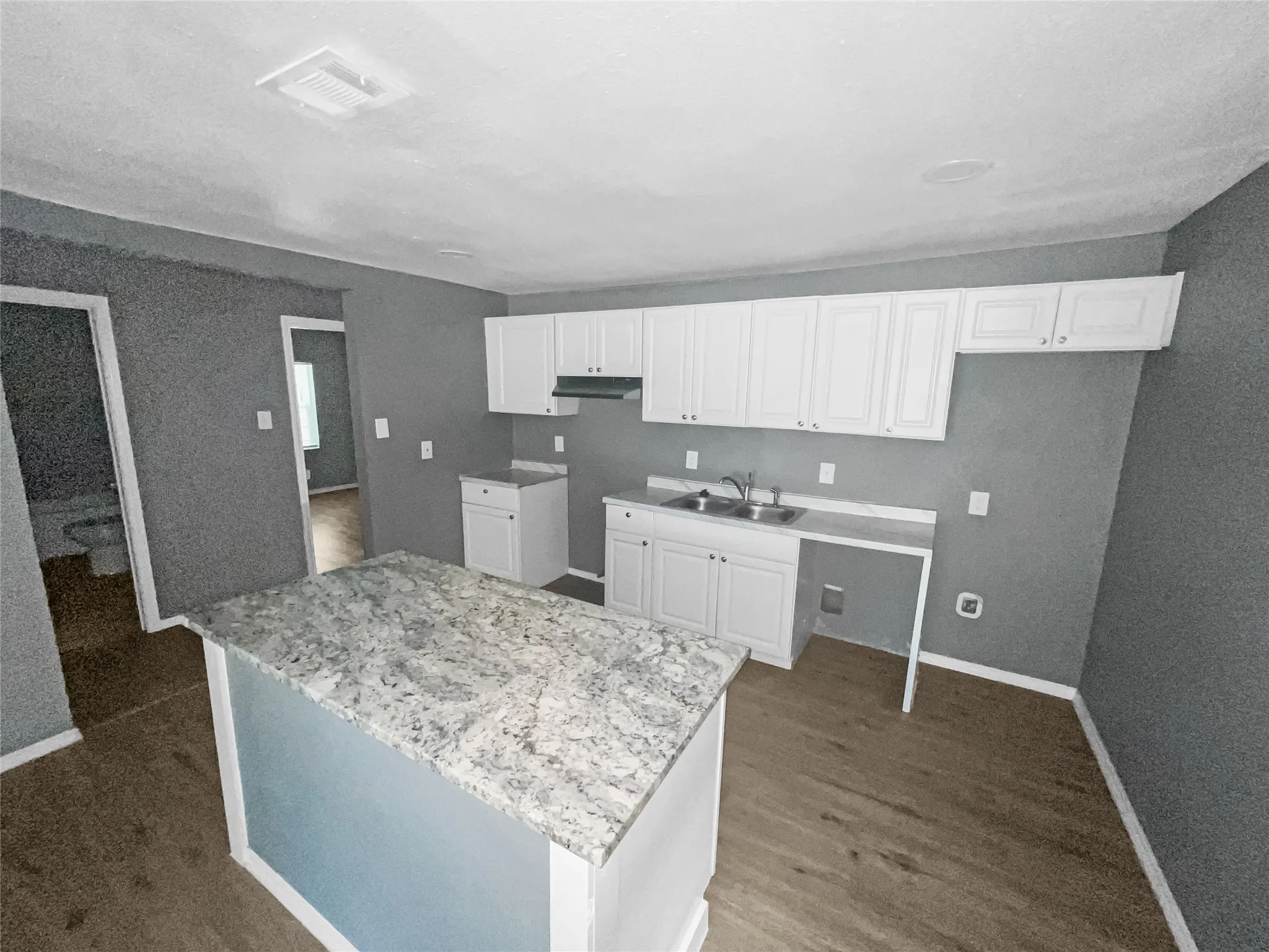 Kitchen featuring white shaker-style cabinetry, a double basin stainless steel sink, and a central island with a light-toned granite countertop