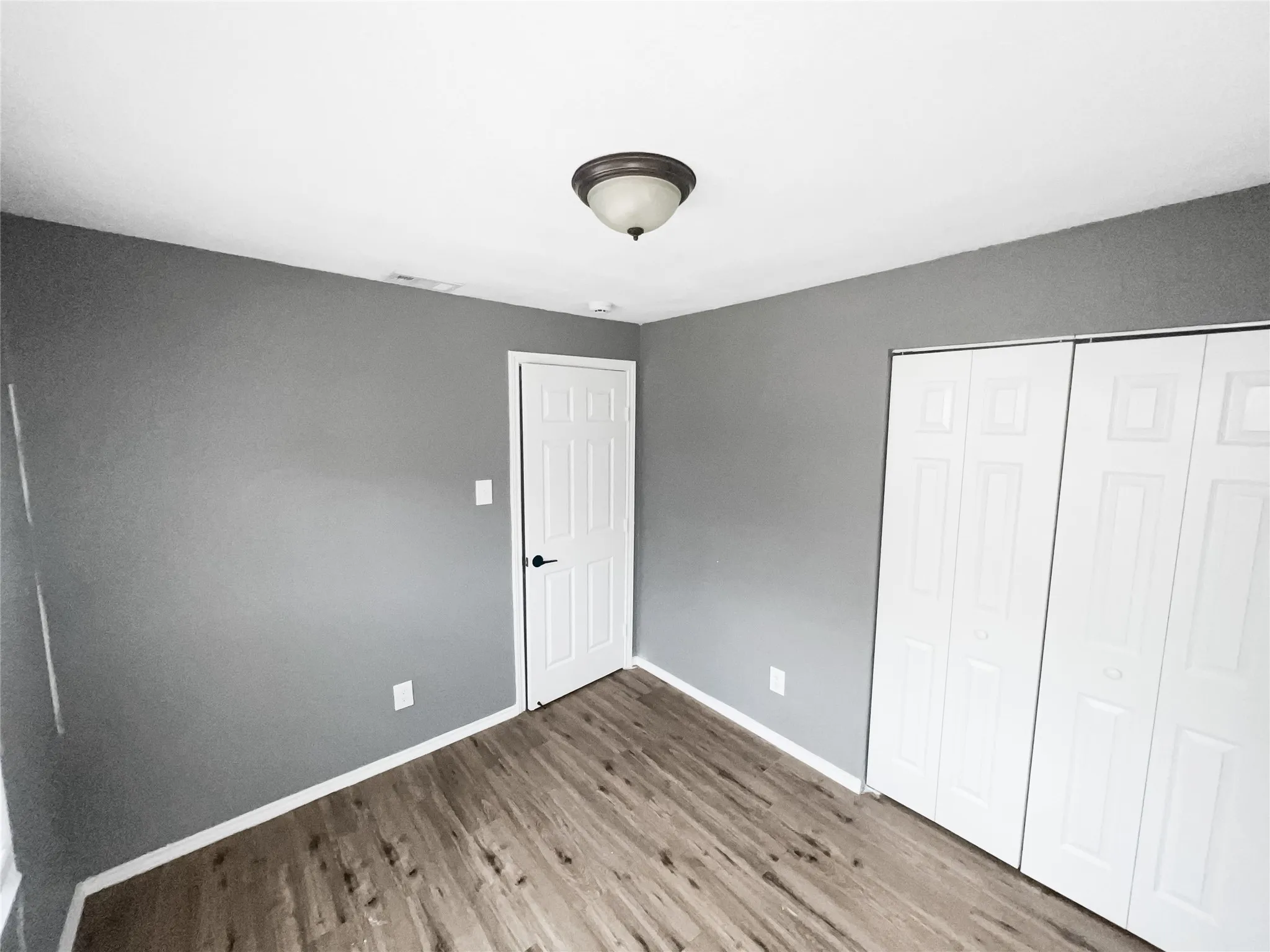 Room featuring wood-finish flooring, neutral gray walls, white baseboards, and a white paneled door with dark hardware