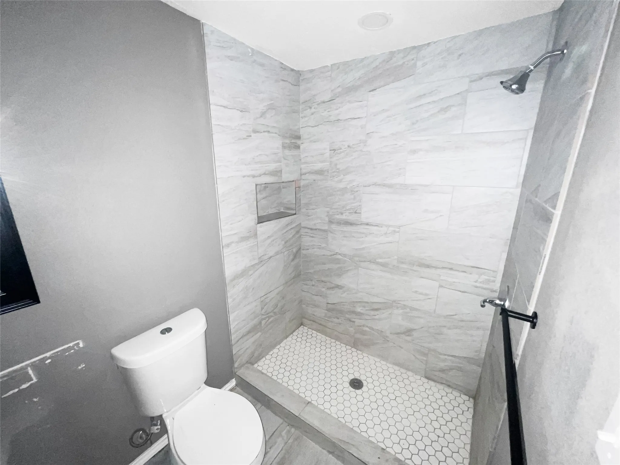 Walk-in shower featuring large format tile walls, a built-in shower niche, and a hexagonal tile floor