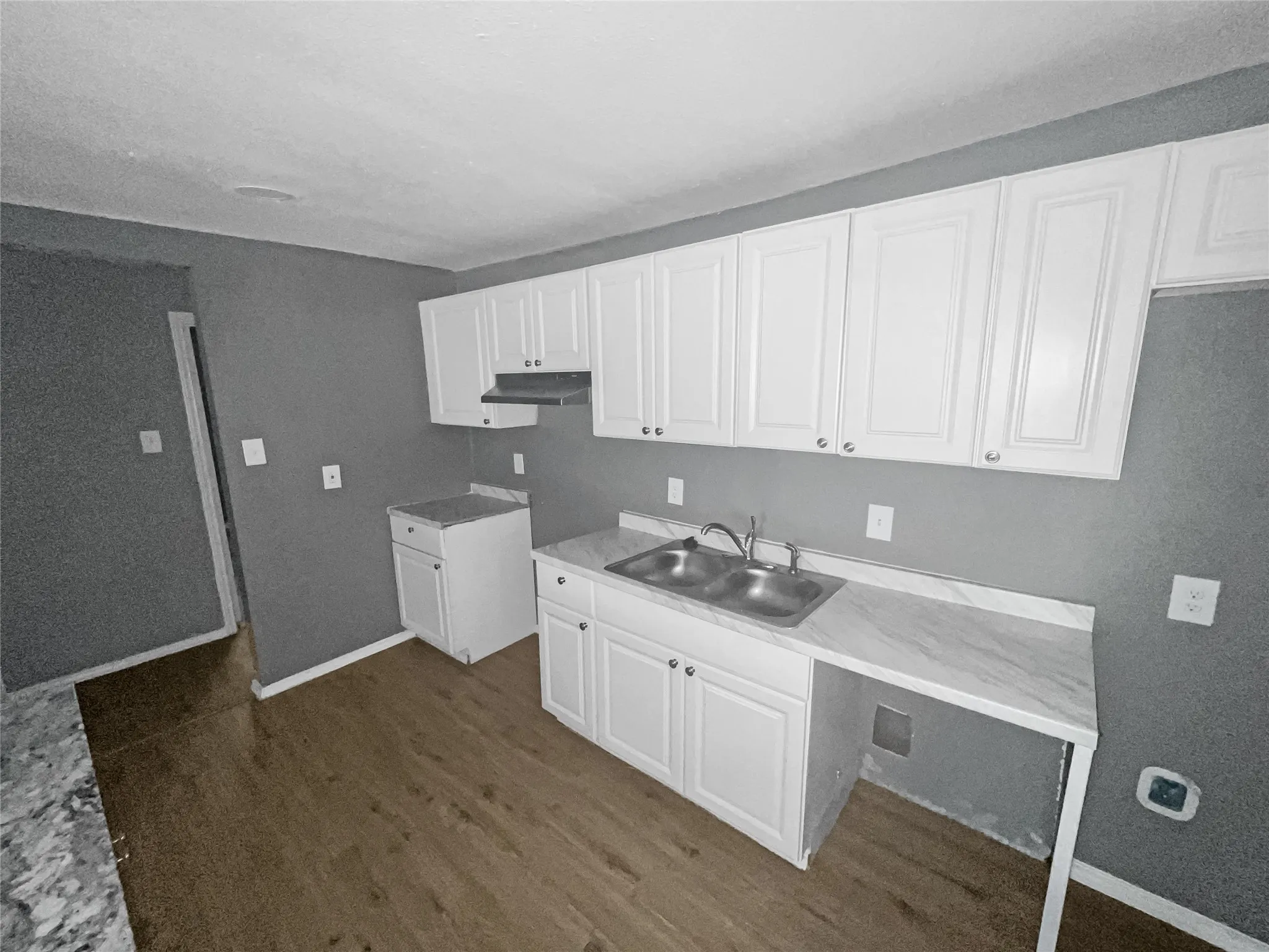 Kitchen featuring white cabinetry, a dual basin stainless steel sink, marbled laminate countertops, and wood-finish flooring
