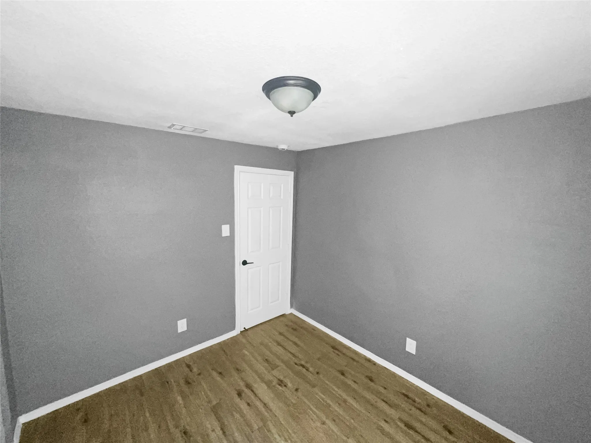 Room featuring wood-finish flooring, neutral gray walls, white trim, and a white paneled door with black hardware