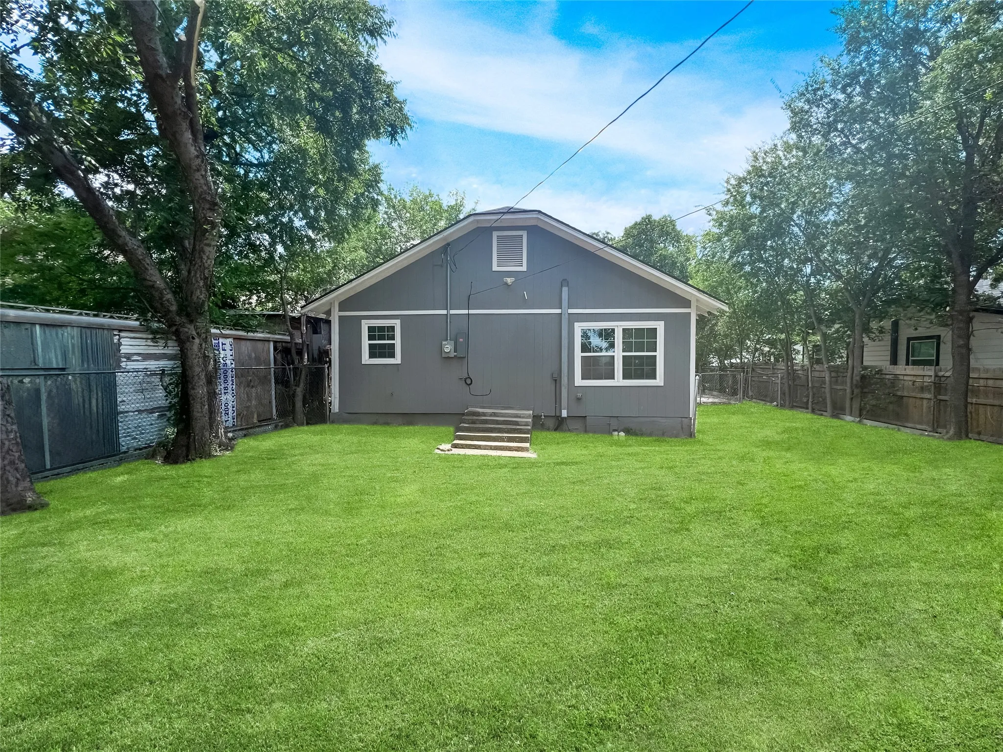 Spacious grassy yard featuring a gray exterior residence with white trim windows and exterior steps