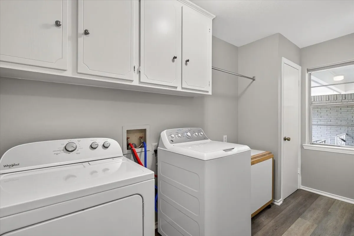 Dedicated laundry area featuring white cabinetry, a built-in hanging rod, wood-finish flooring, and natural light from a window