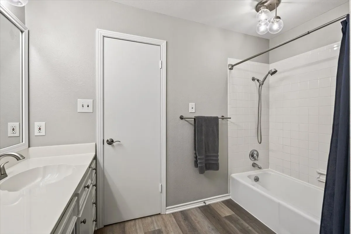 #1 Primary Bathroom showing bedroom access door (closed), combination tub shower, spacious double sink vanity, and bright and airy decor