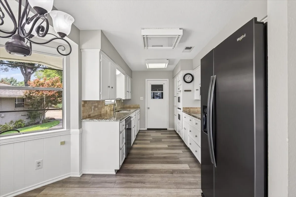Kitchen featuring a dining nook with lake view windows on side of house, white cabinetry, wood-finish flooring, stone countertops, and a full-size black refrigerator