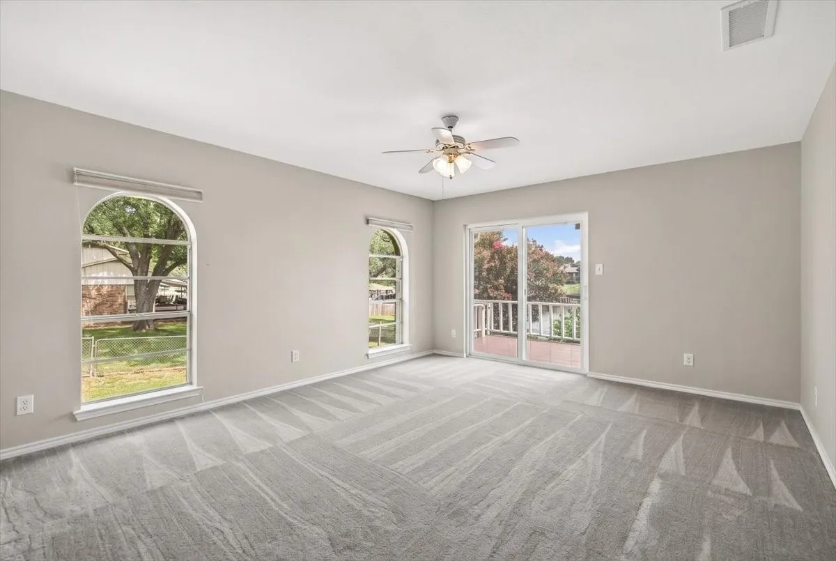 #1 Primary bedroom with access to lake side deck and view of lake.  Featuring arched windows, a sliding glass door, a ceiling fan with integrated lighting.and a sliding glass door opening to an outdoor deck with lake views.