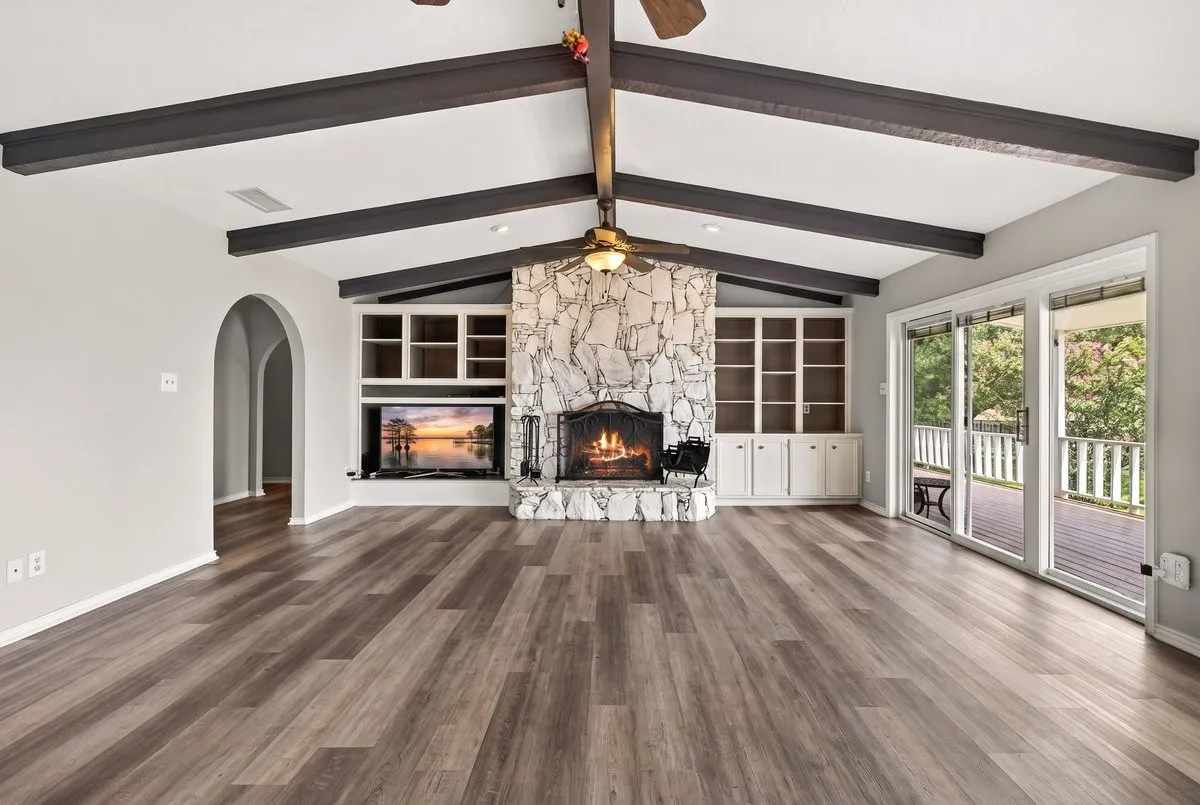 Main Lakeside Living space featuring a stone fireplace with a black metal screen, vaulted ceilings with dark wood beams, and wood-finish flooring