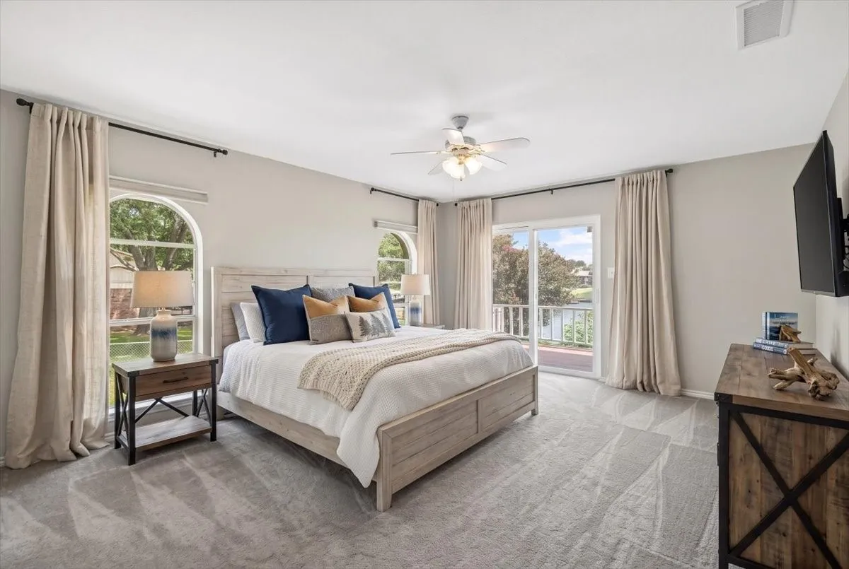 #1 Primary bedroom virtually staged.  Featuring access to lake side deck and view of lake, arched windows, a sliding glass door, a ceiling fan with integrated lighting.