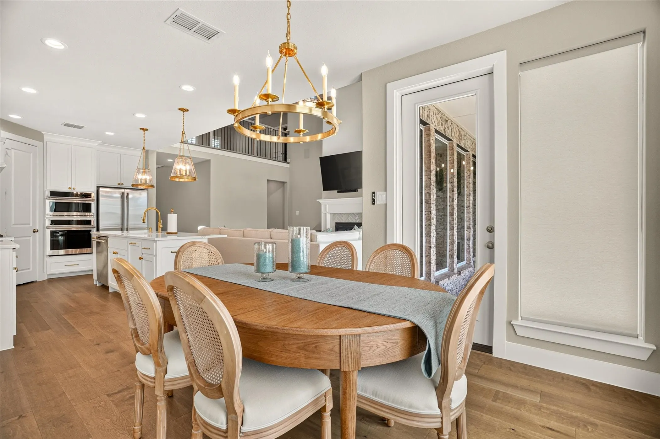 Open-concept dining area featuring wood-finish flooring, a brass chandelier, and direct access to an outdoor patio through a glass-paneled door