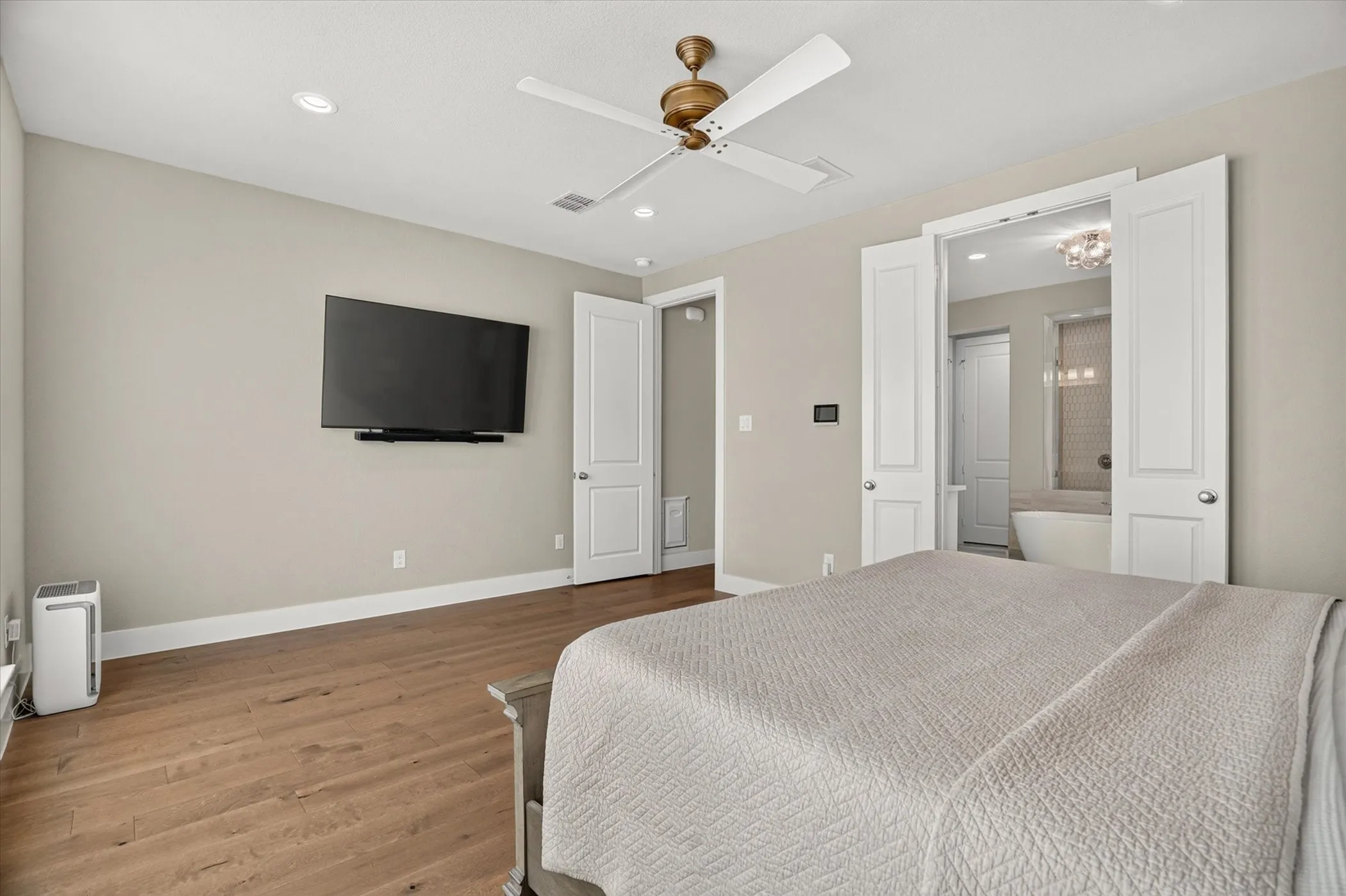 Wood-finish flooring throughout, featuring a ceiling fan with integrated lighting, recessed lighting, and a wall-mounted entertainment system