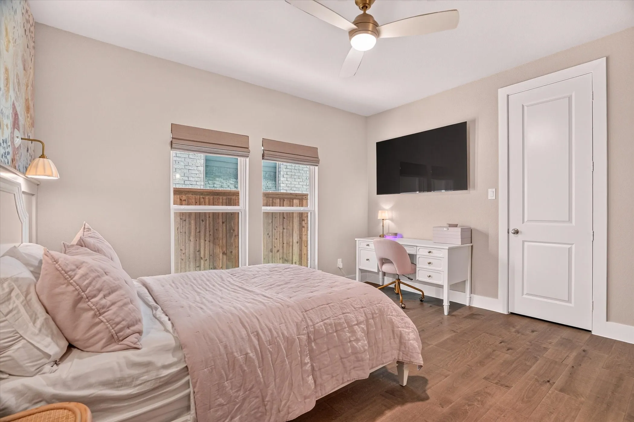 Bedroom featuring wood-finish flooring, two large windows with privacy blinds, a ceiling fan with integrated lighting, and a paneled interior door