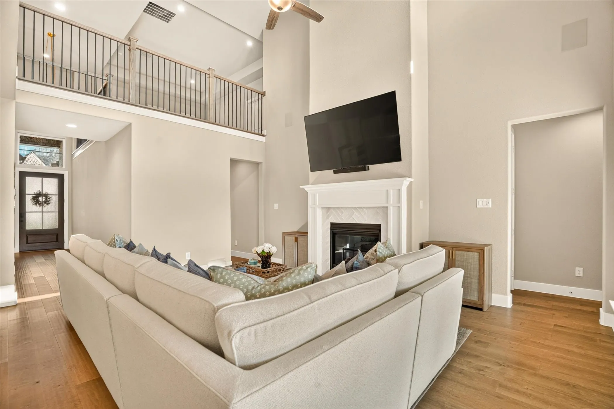 Spacious living area featuring a two-story ceiling, wood-finish flooring, and a fireplace with a white mantel and herringbone tile surround
