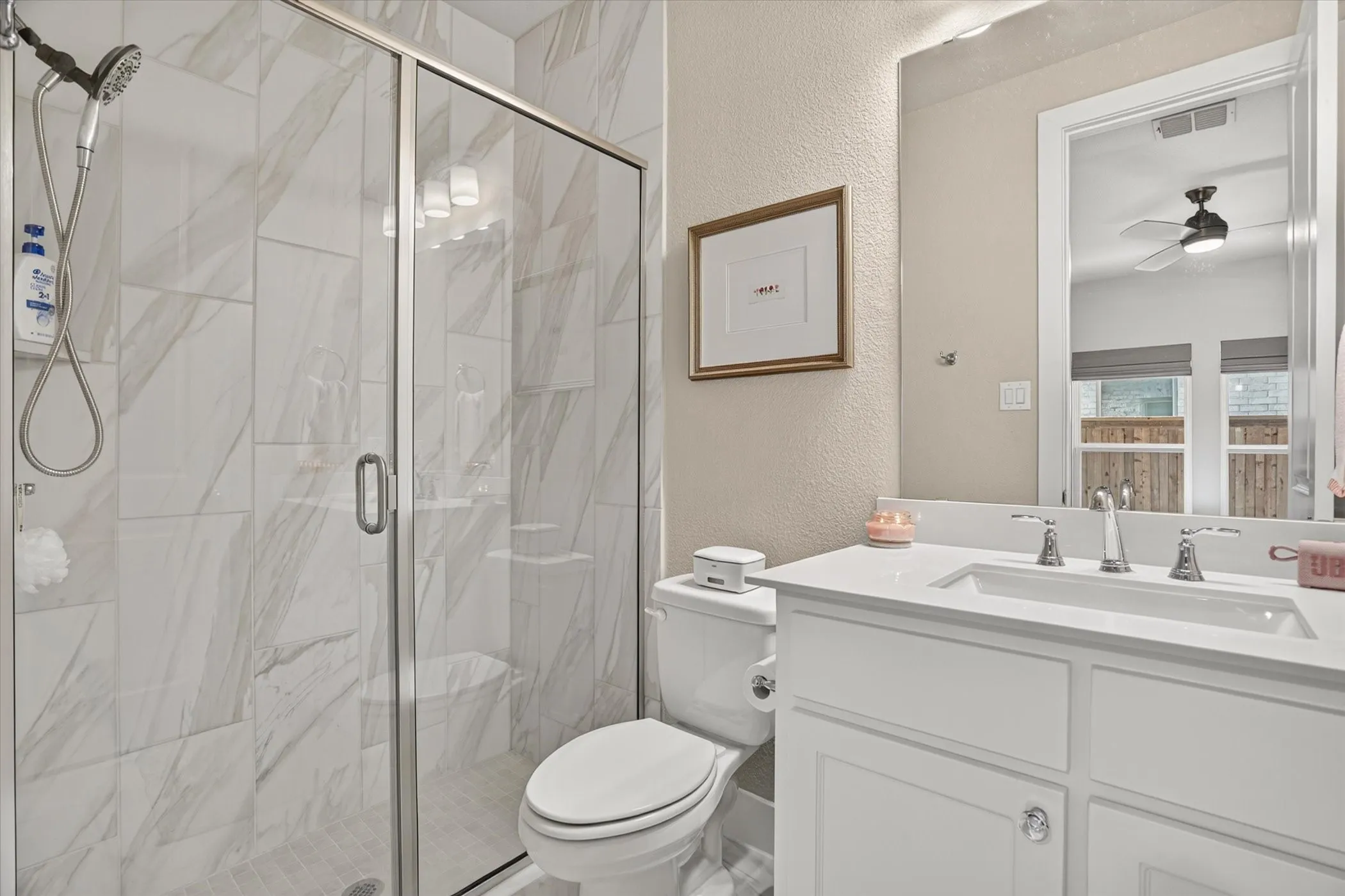Bathroom featuring a glass-enclosed shower with white and gray tiled walls, a white vanity with an integrated sink and chrome fixtures, a large wall-mounted mirror, and a white toilet