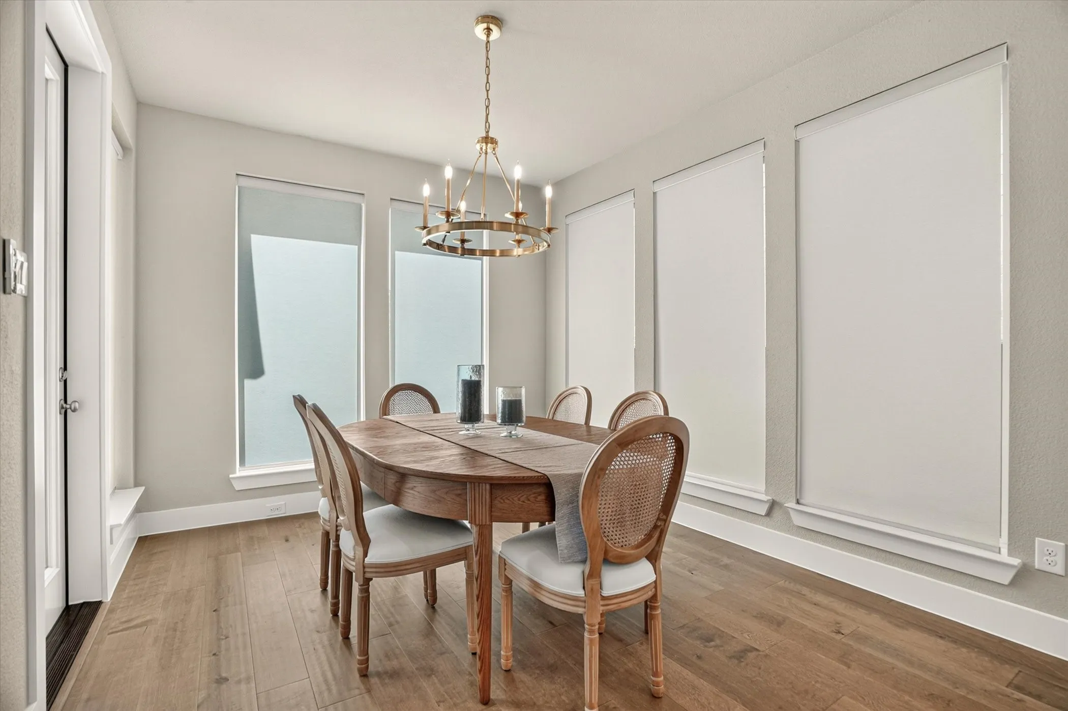Dining space featuring wood-finish flooring, a gold-toned chandelier, multiple windows with roller shades, and light-toned wall paint