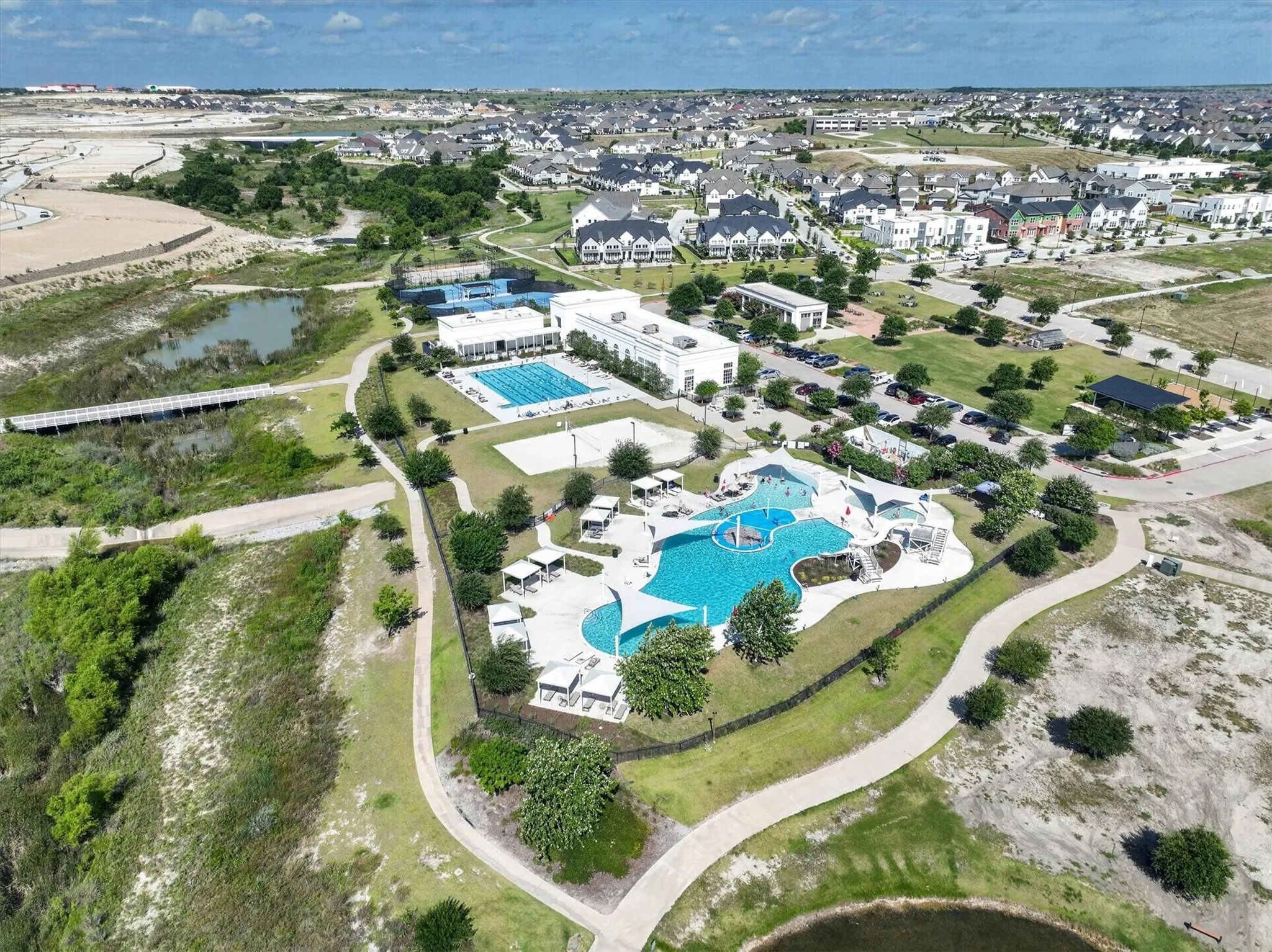 Expansive community recreation area featuring a resort-style pool with shaded lounge areas, a rectangular lap pool, tennis courts, and landscaped walking paths